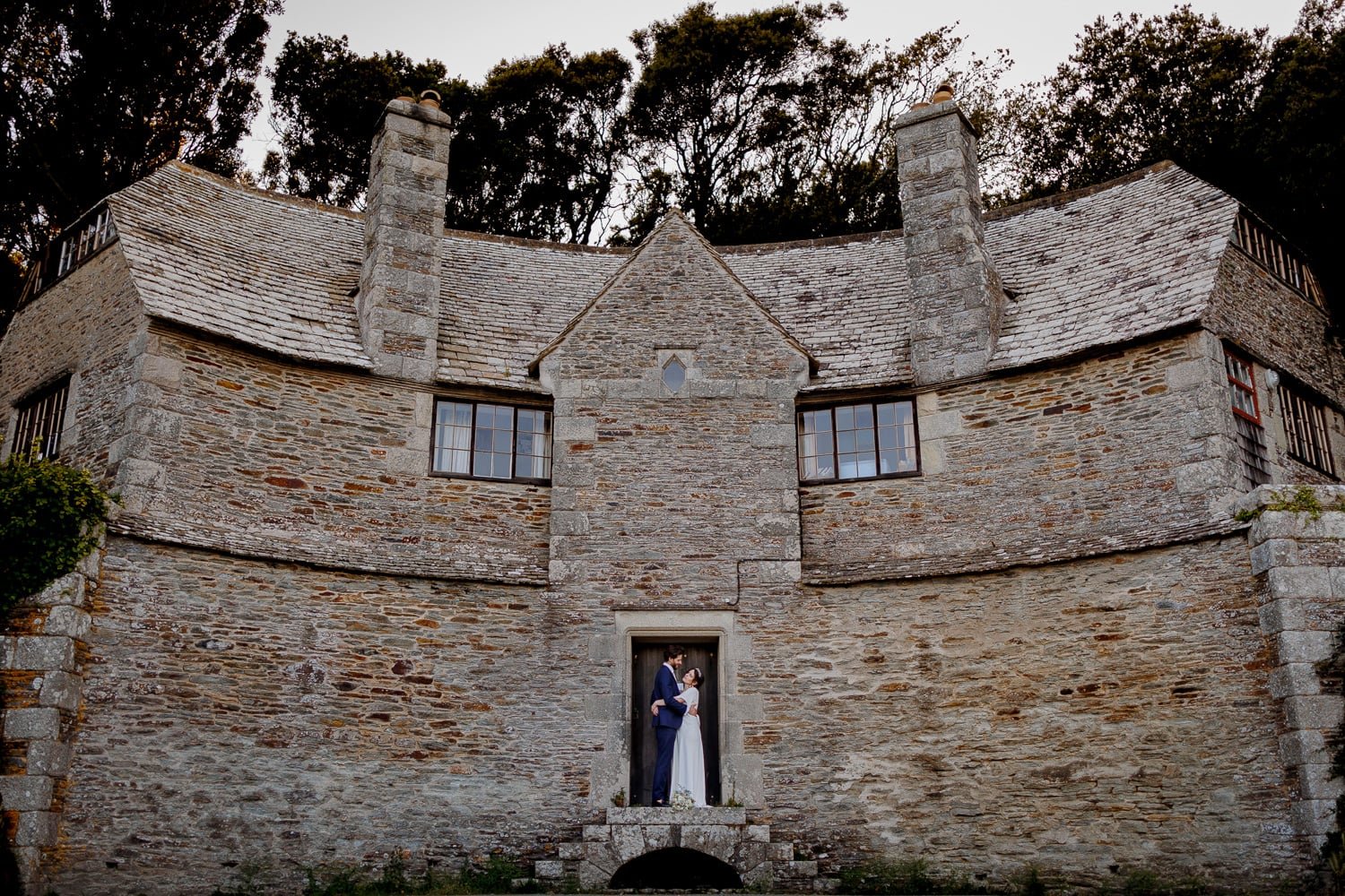A bride and groom standing in the doorway of a stone castle or historic building, looking at each other.