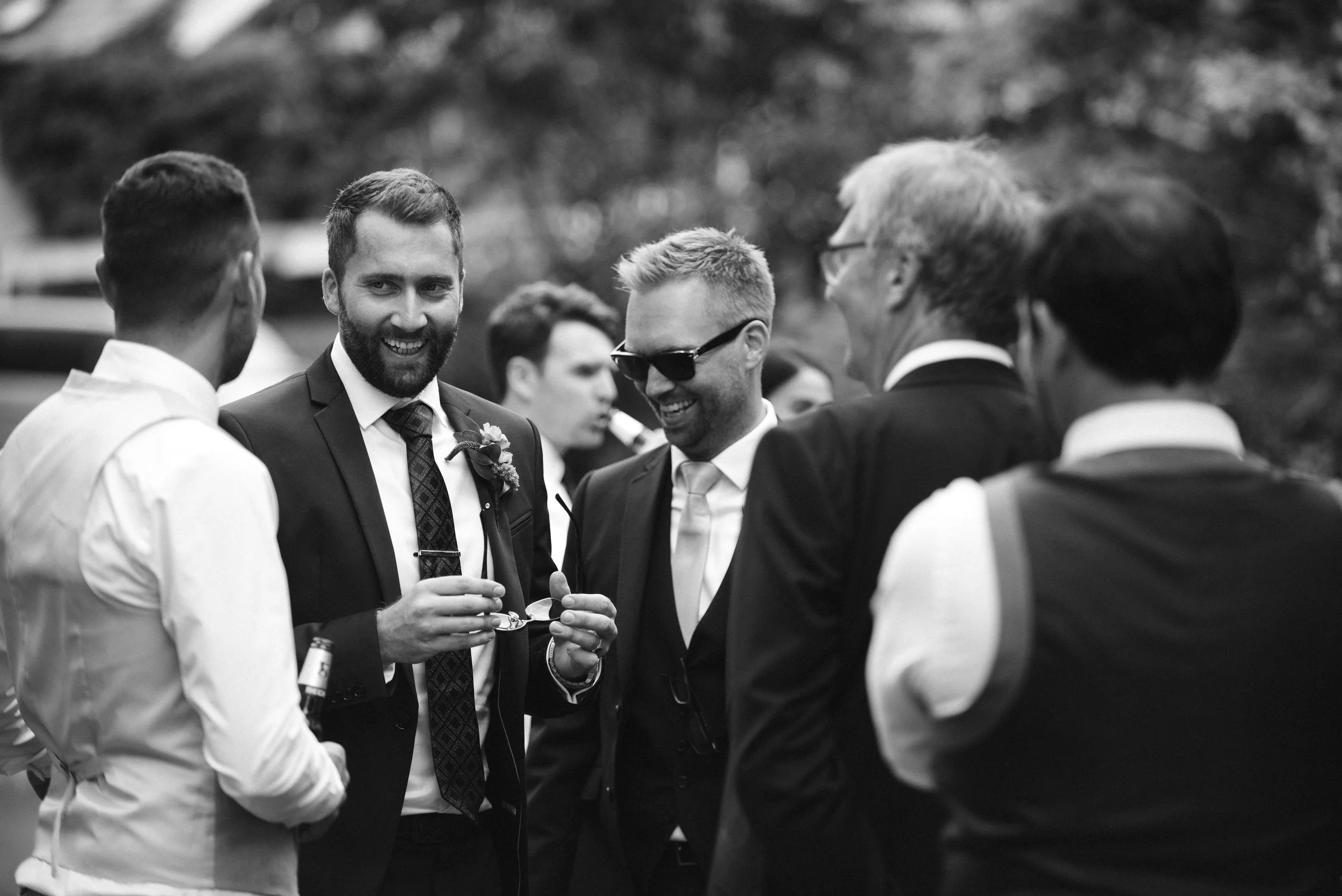 Group of men in suits and vests socializing outdoors, smiling and talking.