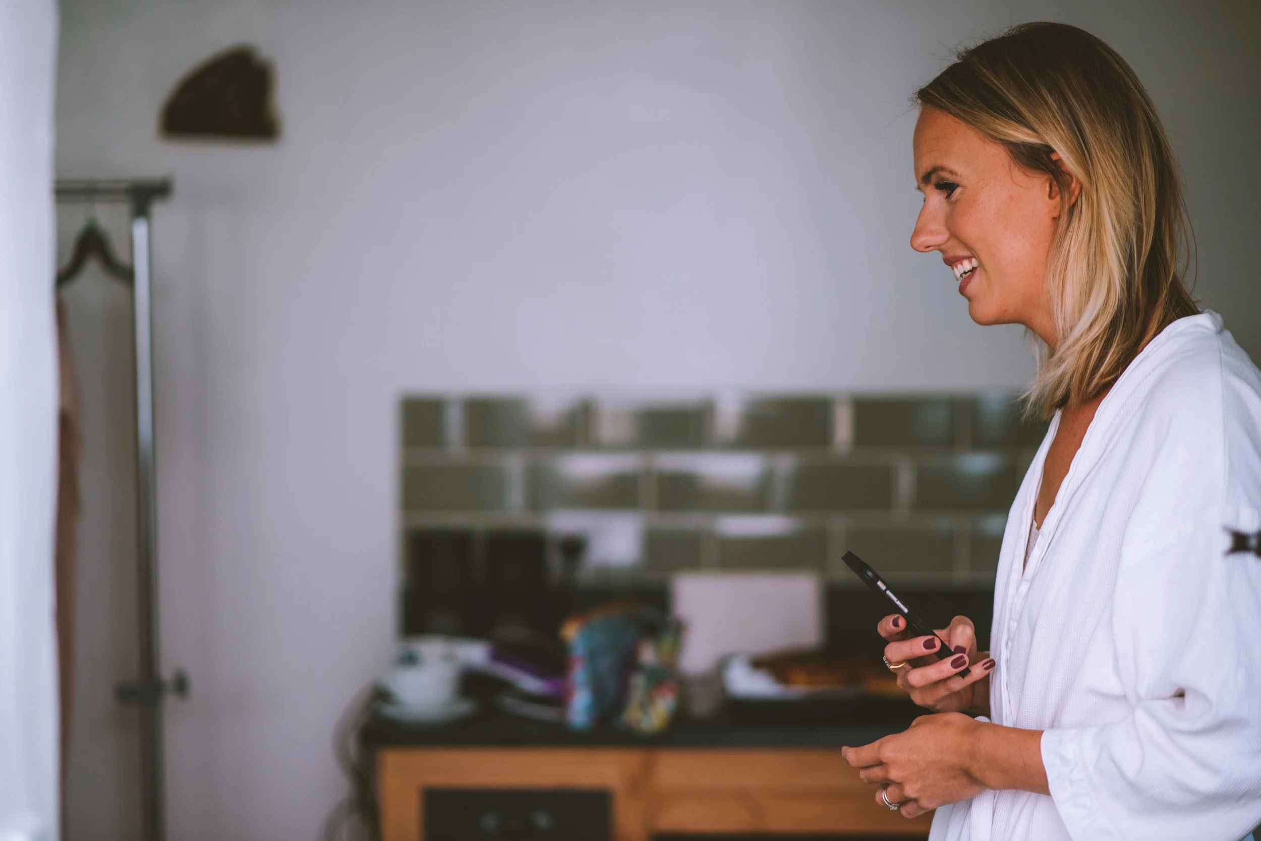 A woman in a white blouse holding a phone, smiling and looking towards the left.