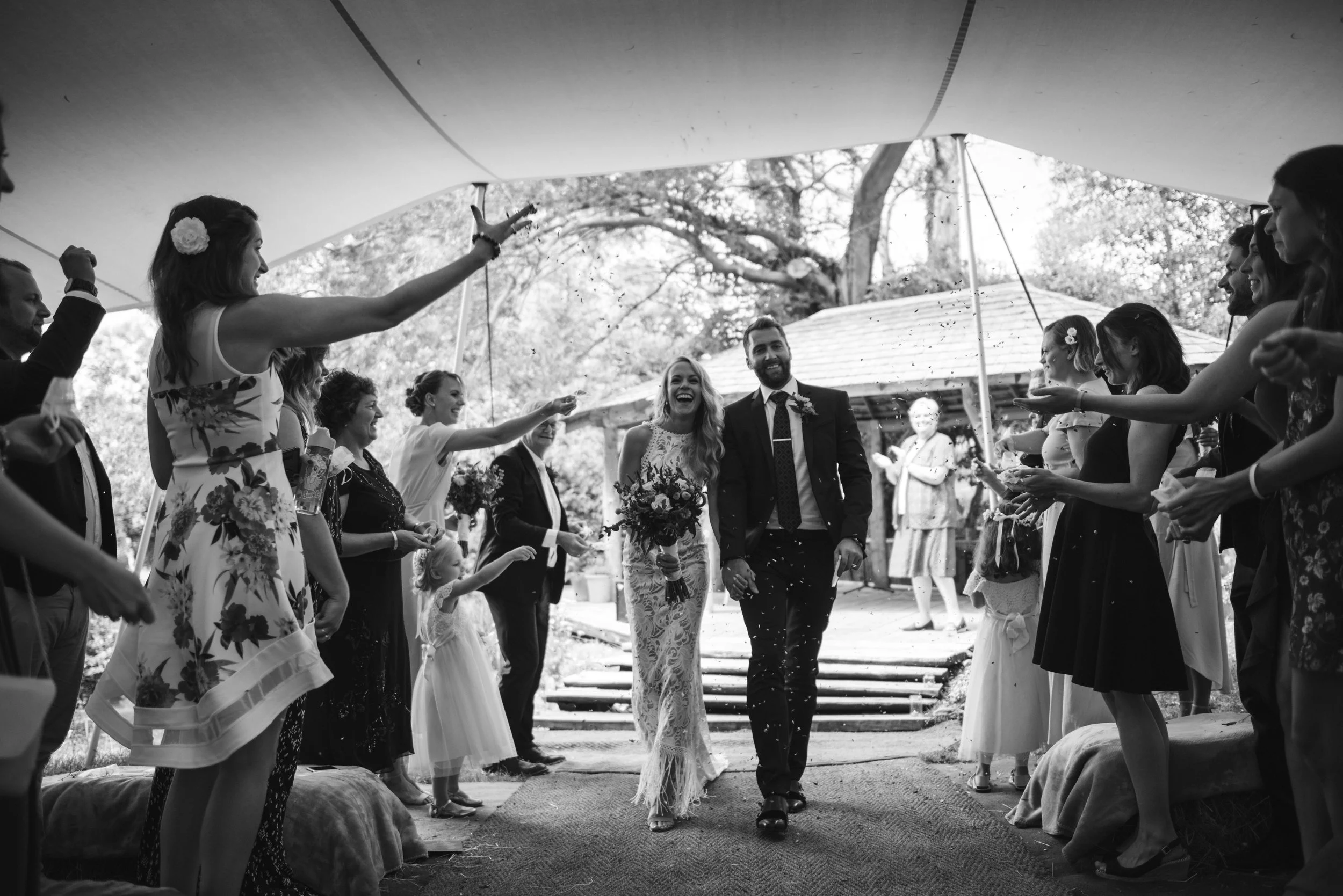 Bride and groom walking down the aisle surrounded by wedding guests under a canopy, celebrating their wedding.