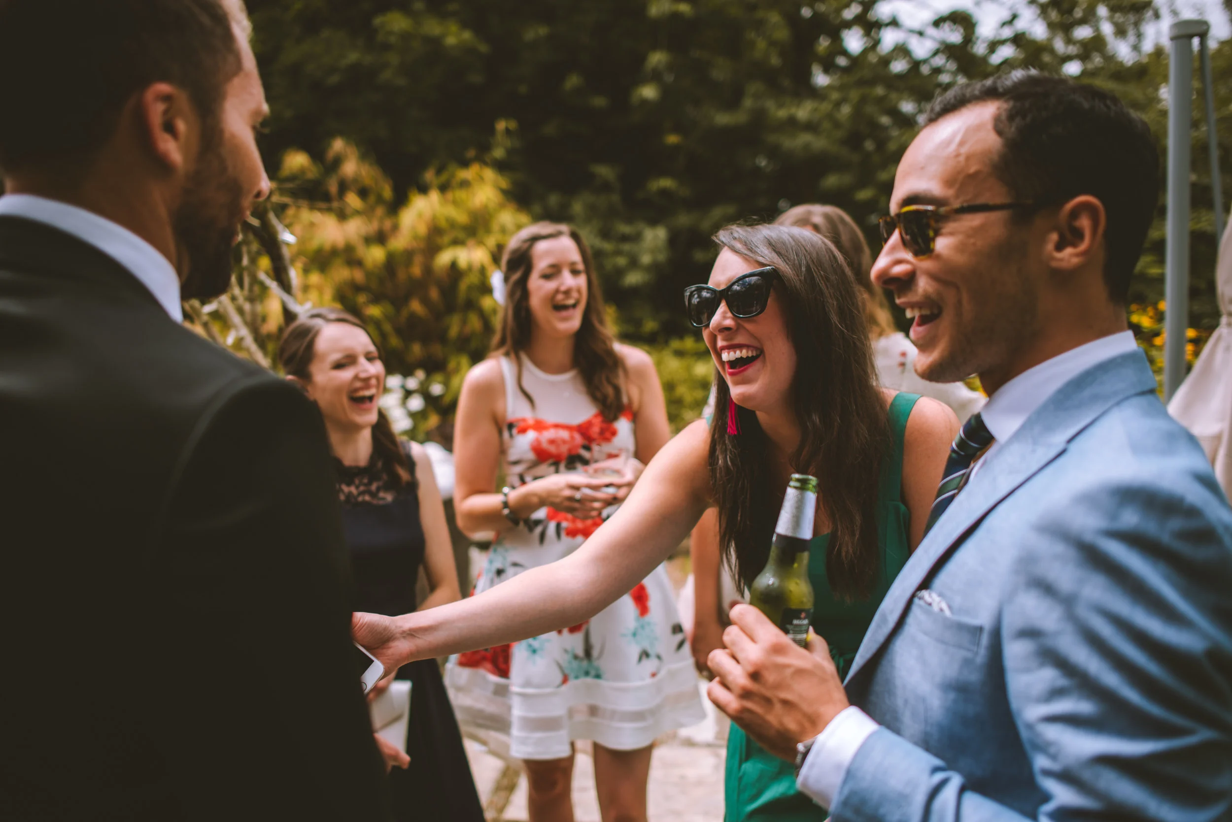 People laughing and socializing outdoors, some wearing sunglasses, at a gathering or party.