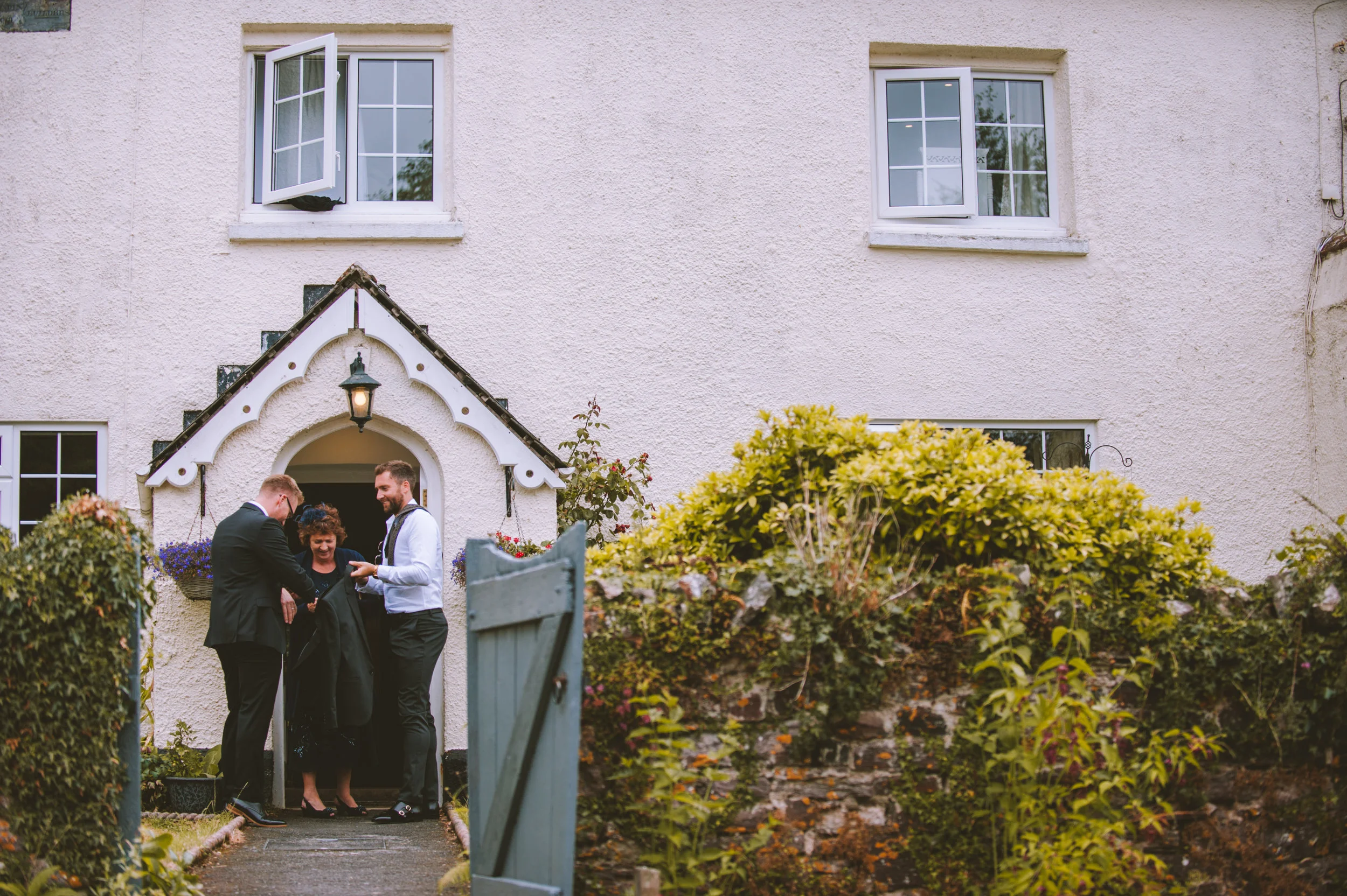 A group of four people, dressed in formal attire, standing at the entrance of a white stucco house, smiling and sharing a moment outside.