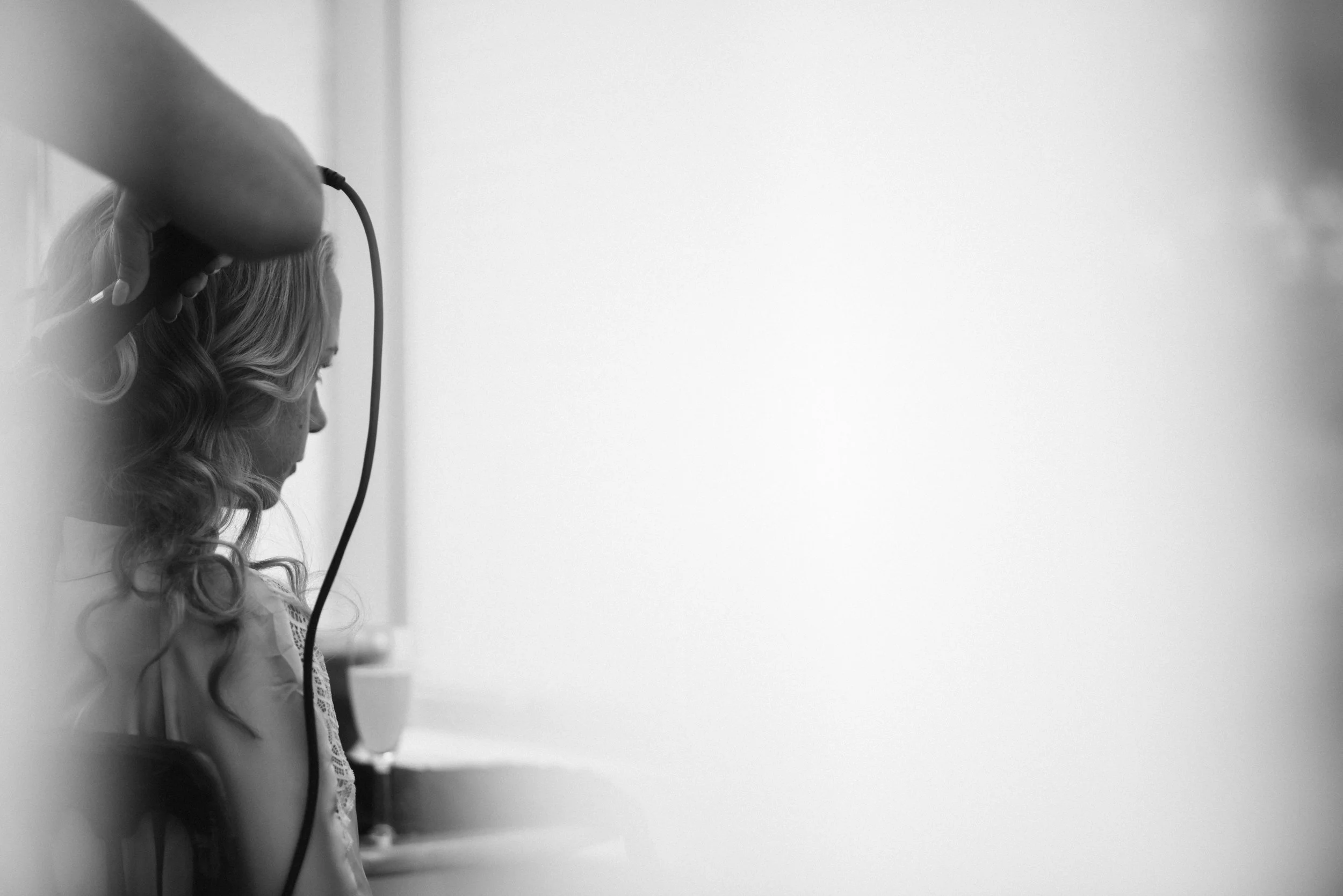 A woman with long, curly hair having her hair styled with a curling iron, in black and white.