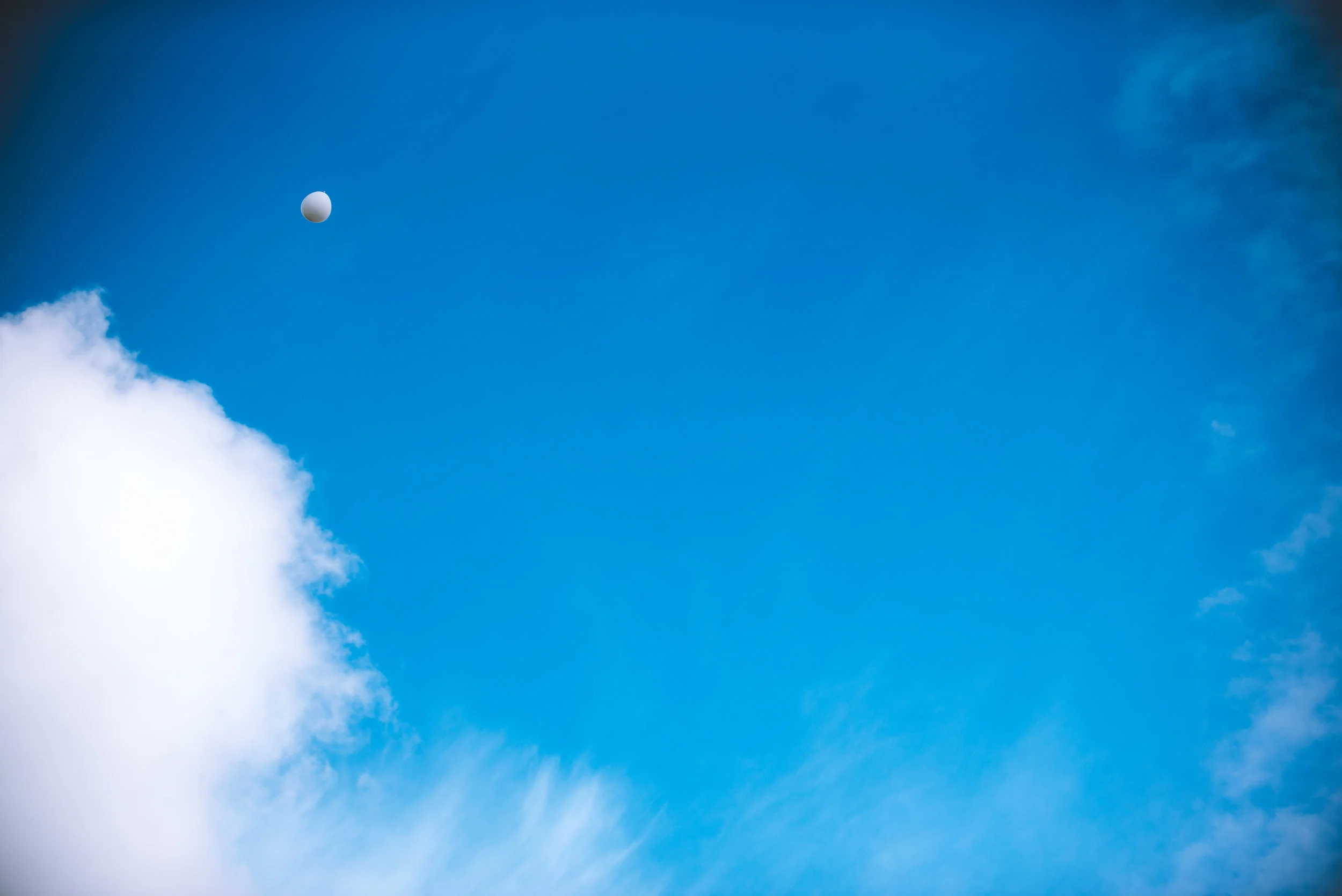 Blue sky with white clouds and a visible moon in the upper left corner.