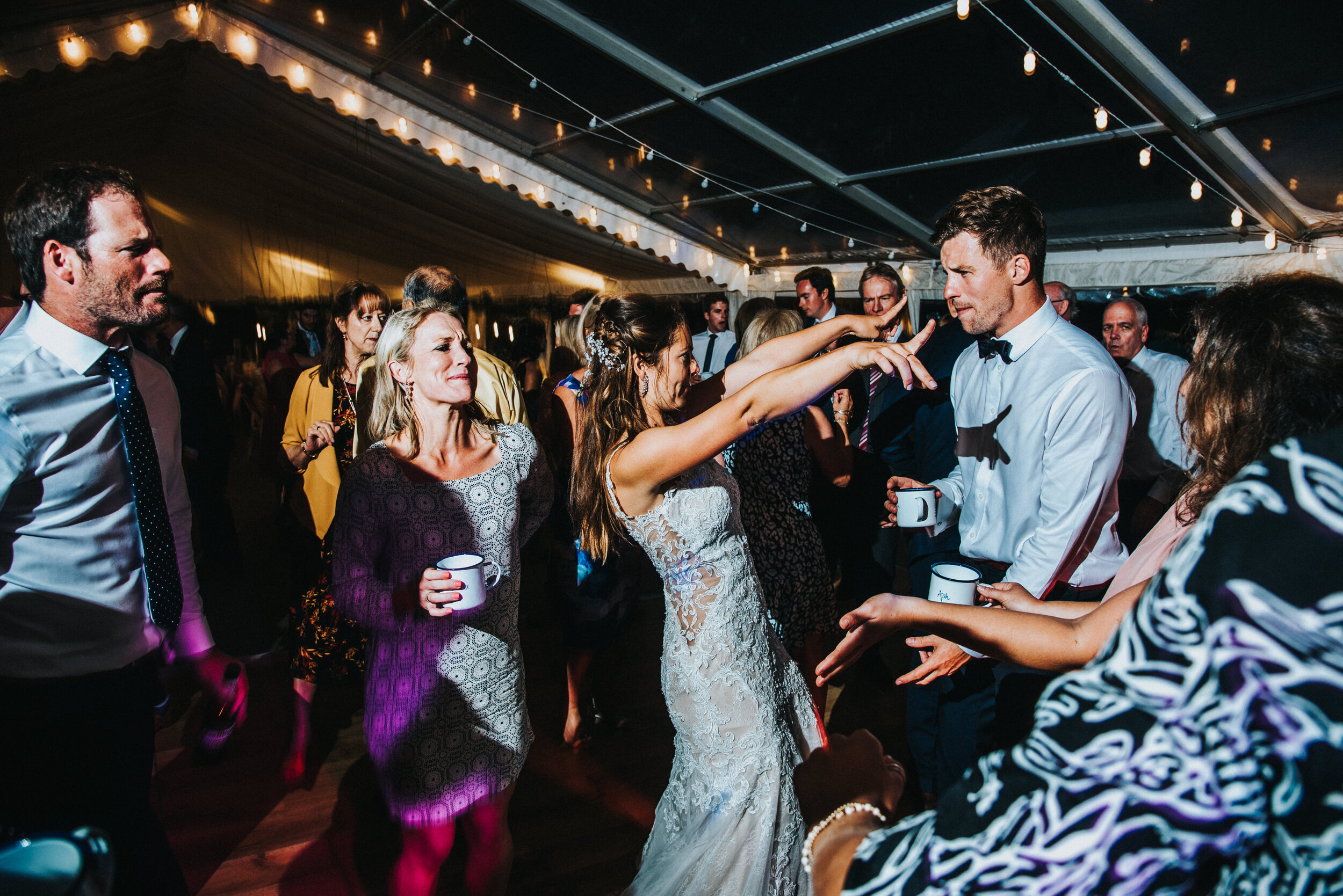 Daymer bay wedding photography captured by Cornwall wedding photographer Mark Shaw Photography - first dance photo. People dancing and socializing at a wedding reception inside a decorated tent, with string lights hanging from the ceiling.