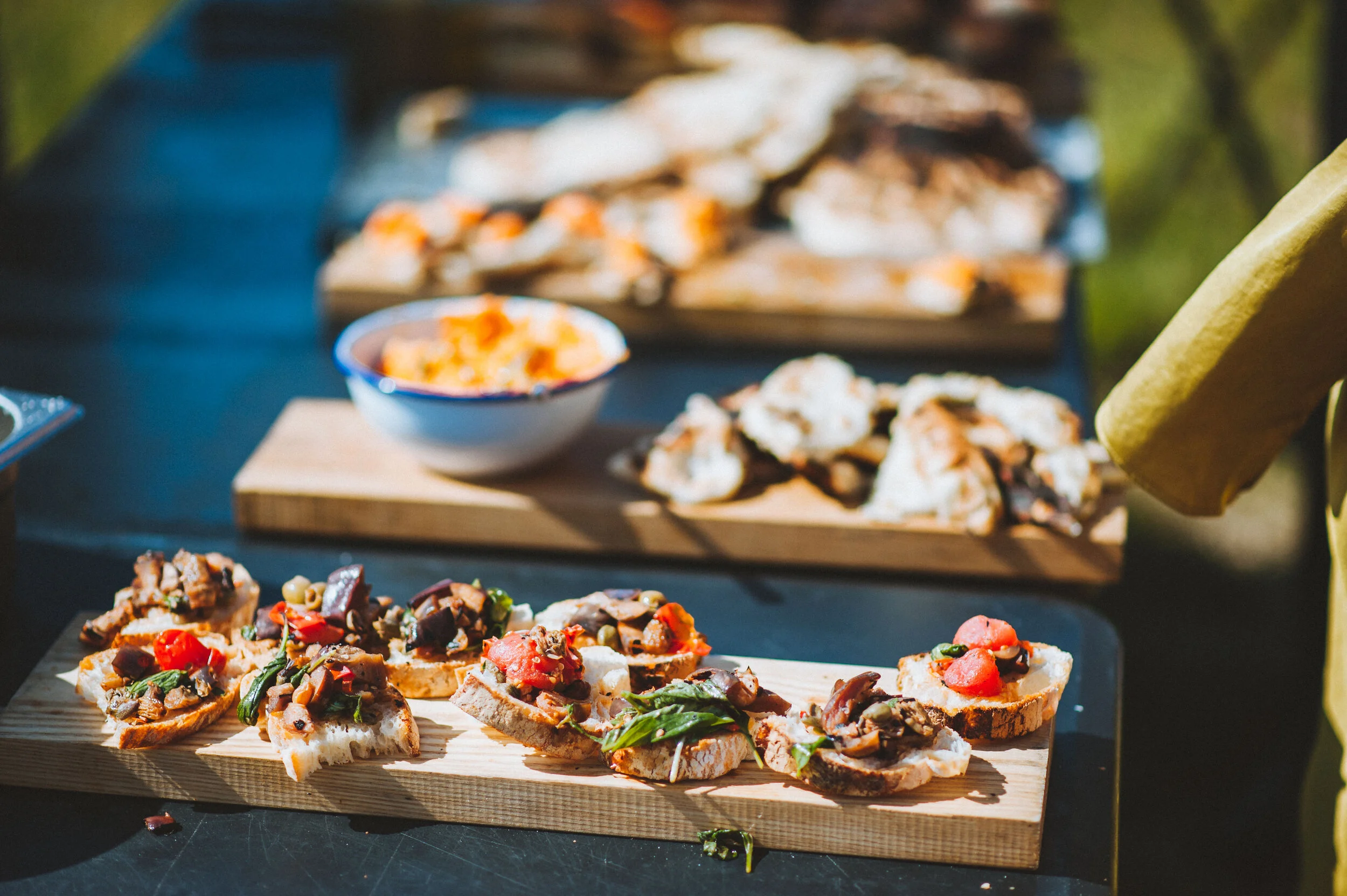 Wedding photo at Greenaway Field in Cornwall. Assorted bruschetta appetizers topped with tomatoes, mushrooms, and herbs on a wooden serving board.
