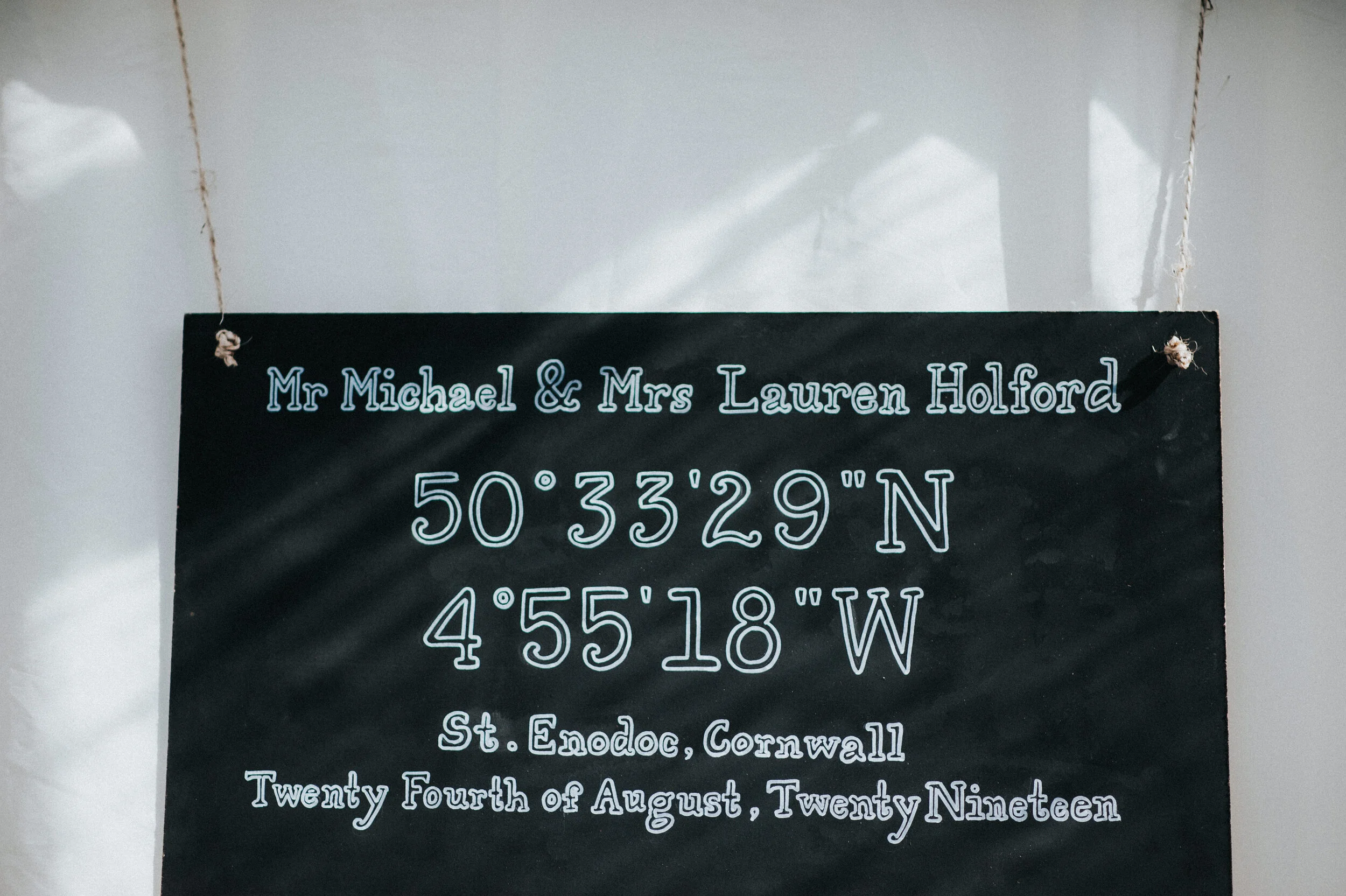 Daymer bay wedding photography in Cornwall captured by MarA black hanging sign with white and blue text indicating the names Mr. Michael and Mrs. Lauren Holford, coordinates 50°33'29"N 4°55'18"W, located in St. Eadoc, Cornwall, dated August 24, 2019.