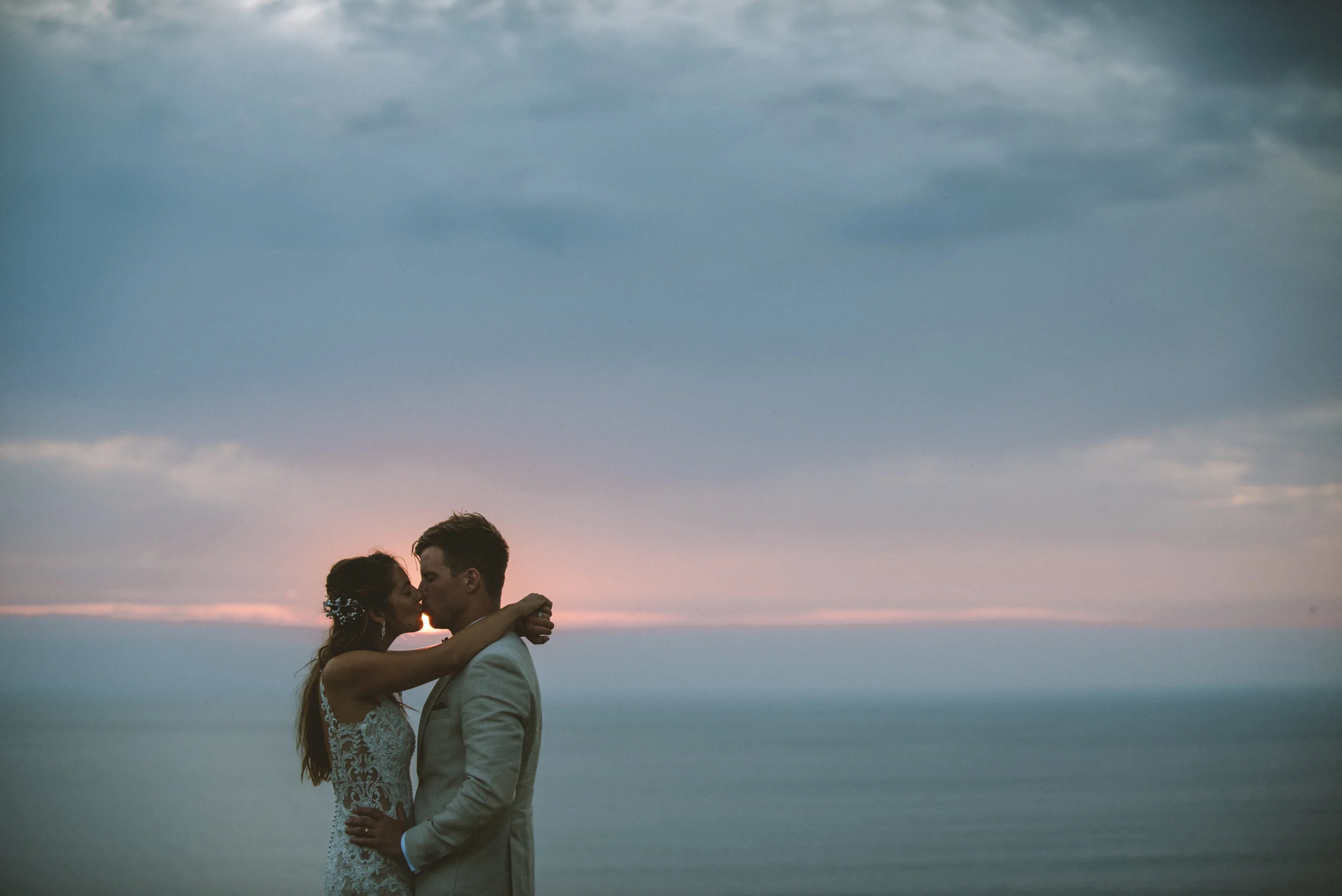 Daymer bay wedding photography captured by Cornwall wedding photographer Mark Shaw Photography - A couple dressed in wedding attire sharing a kiss at sunset by the ocean