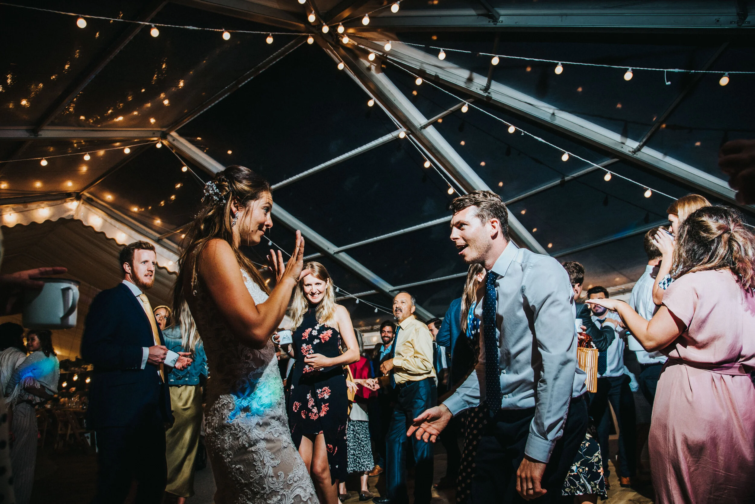 Daymer bay wedding photography captured by Cornwall wedding photographer Mark Shaw Photography -People dancing at a wedding reception under string lights in a large tent.