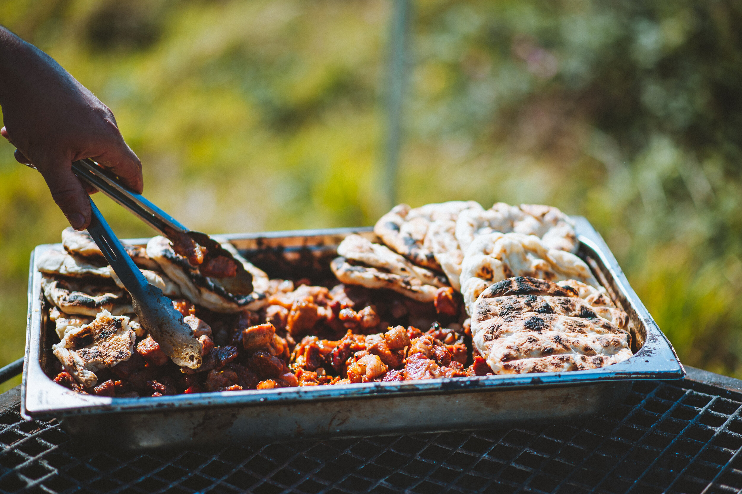 Wedding photo at Greenaway Field in Cornwall. Person serving grilled meats and flatbread from a tray outdoors.