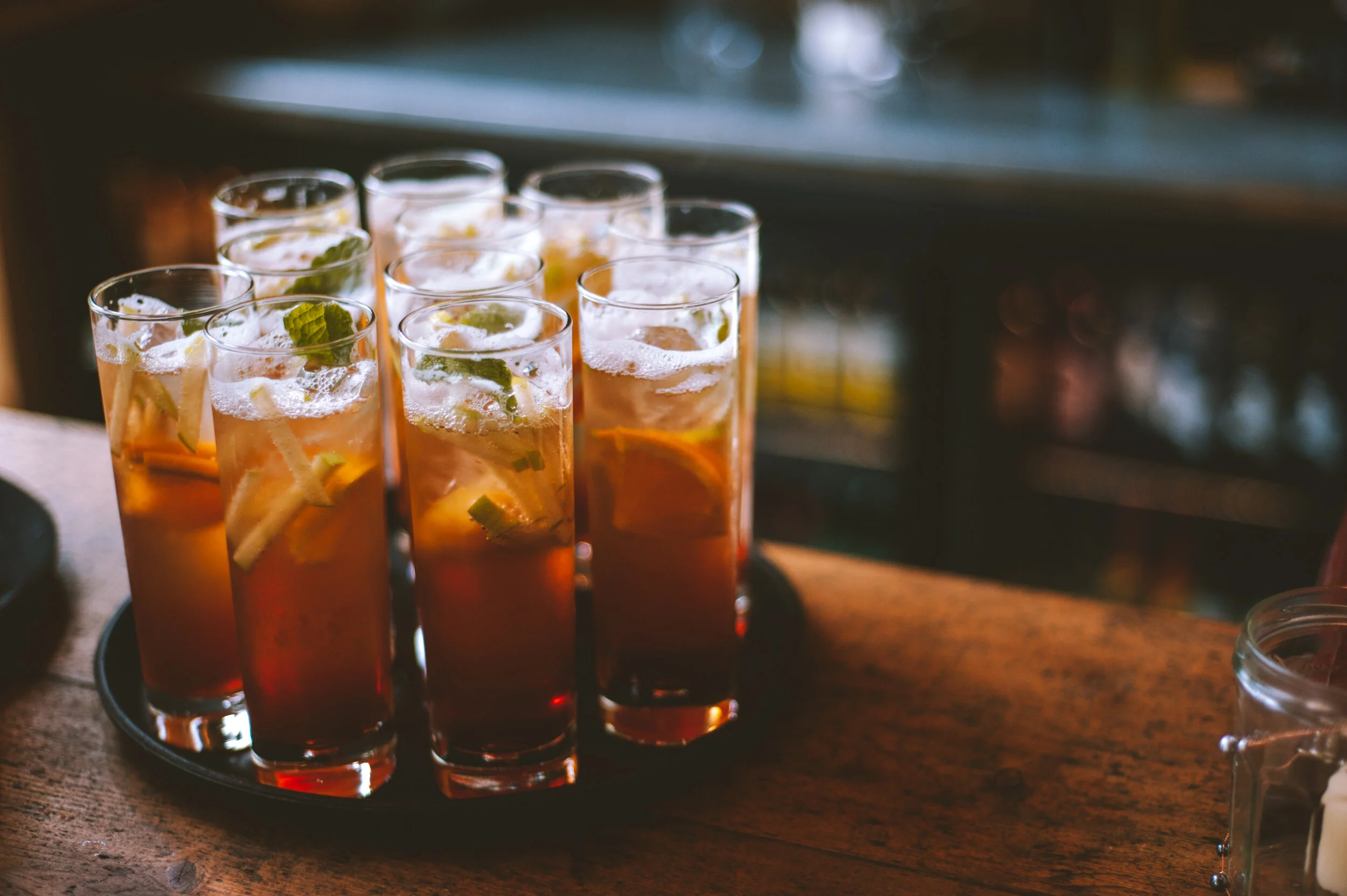 Tray of iced cocktails with lemon slices and mint, on a wooden bar.