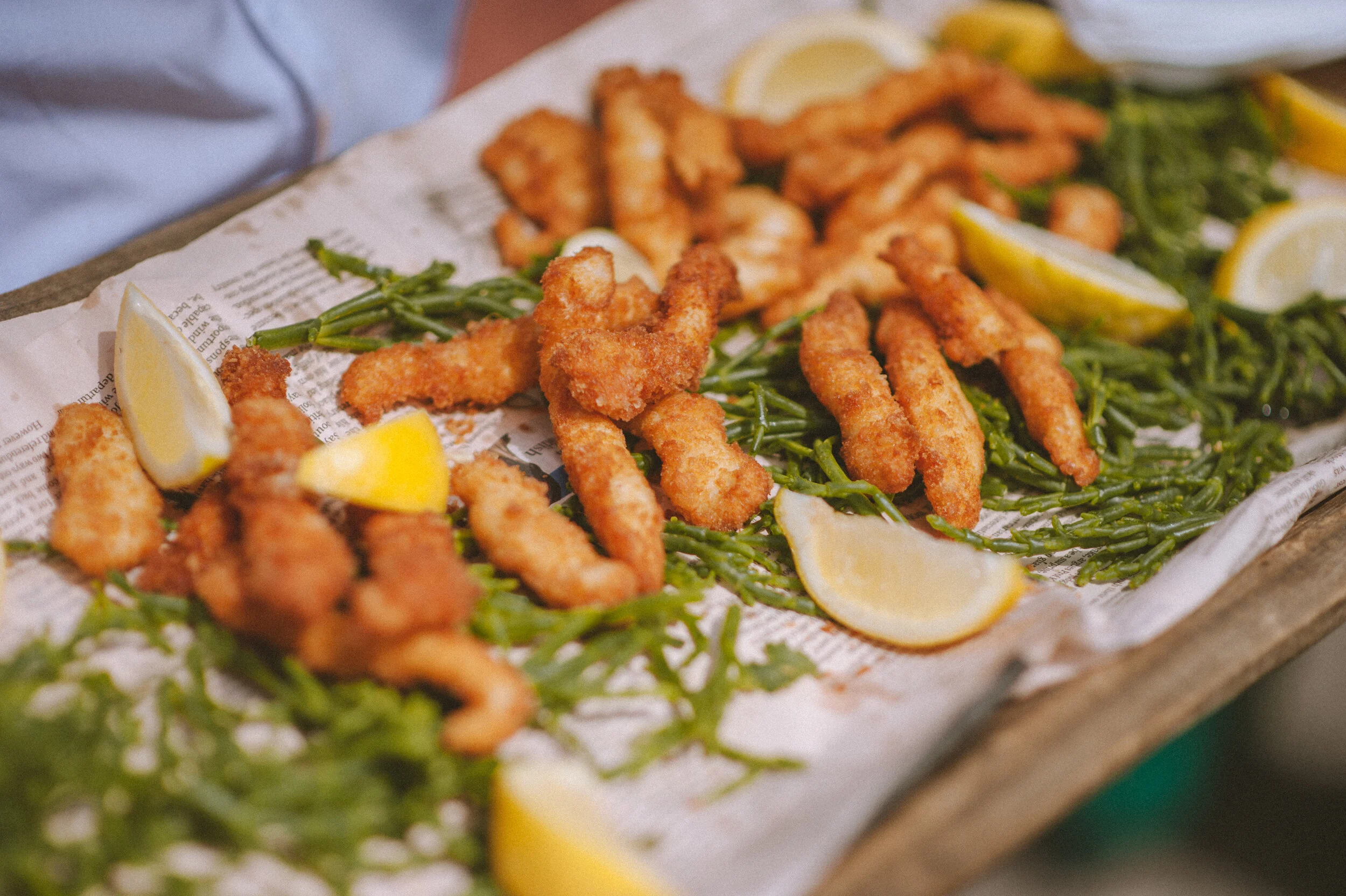 Photo of wedding food - fried seafood with lemon wedges on seaweed and newspaper tray.
