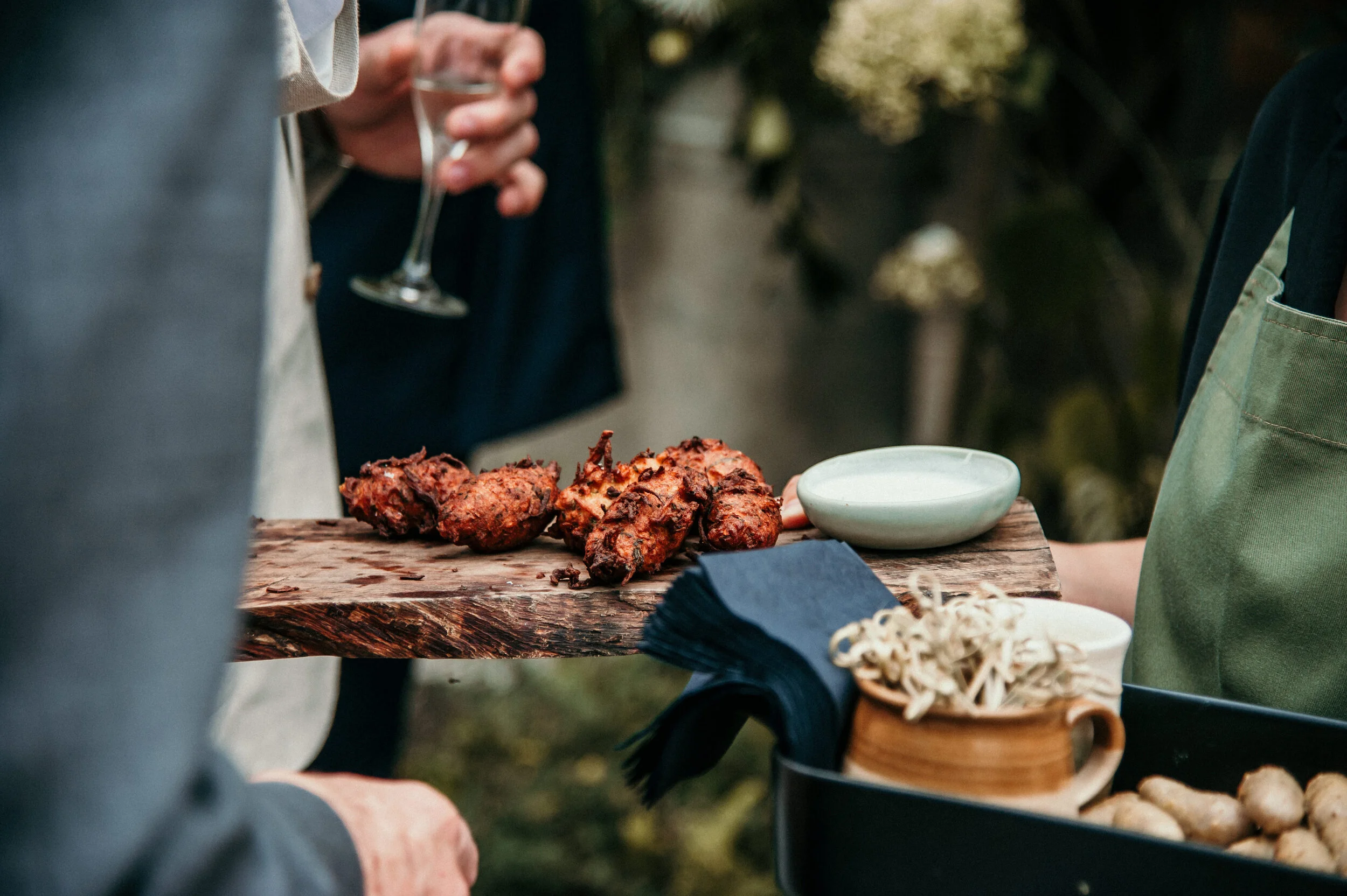 Person holding a tray with fried food, sauce, and garnishes at an outdoor gathering.
