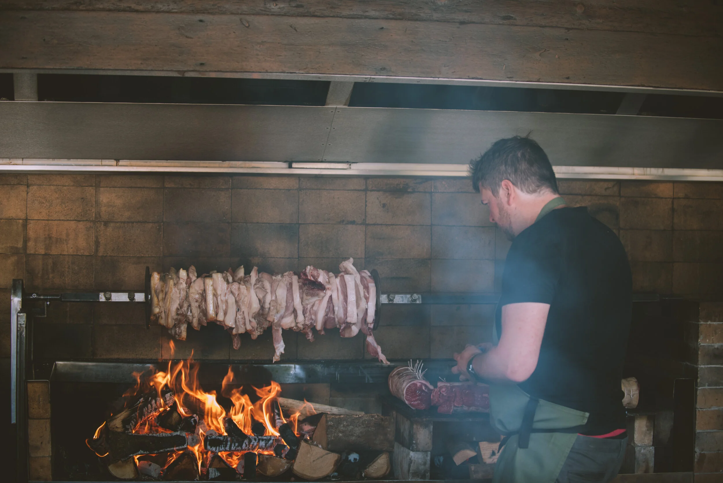 Person grilling meat on a rotisserie over open fire