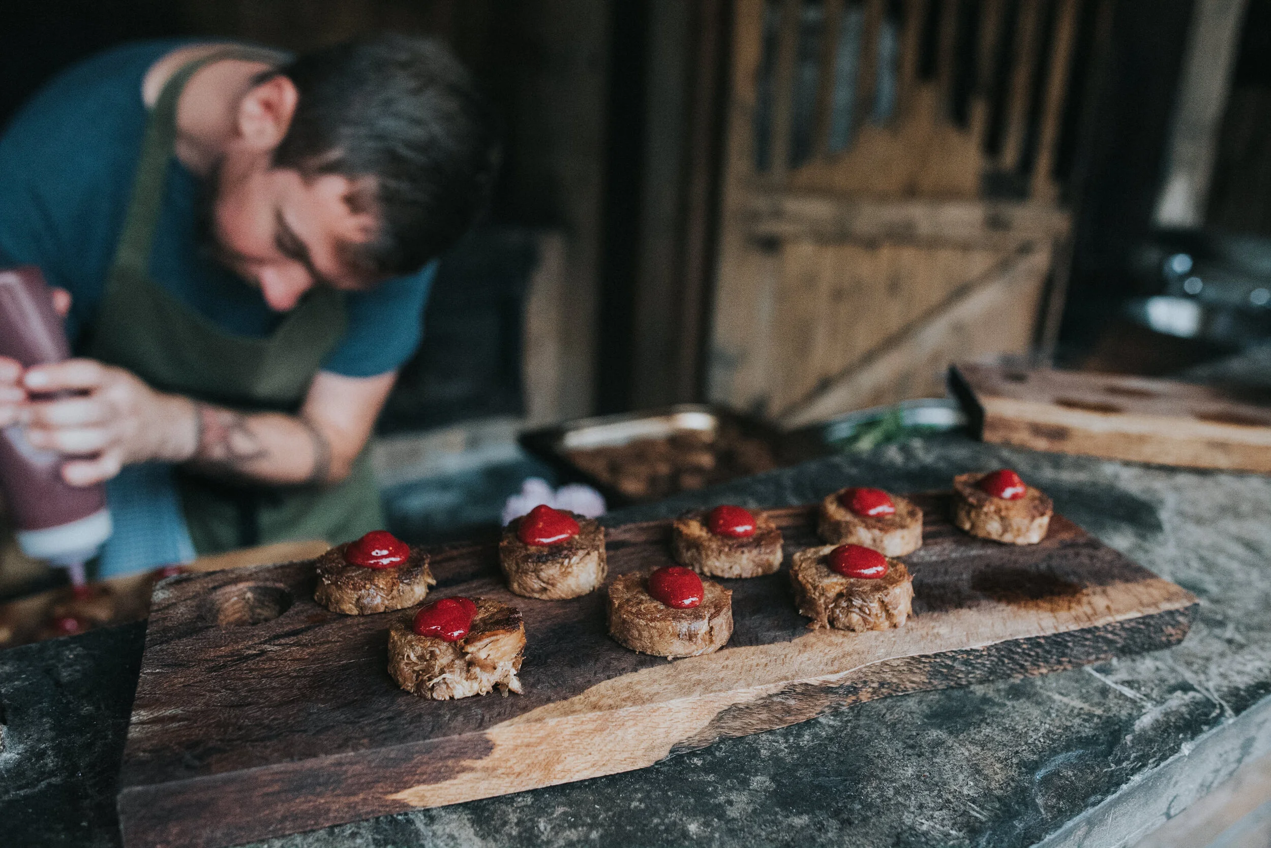 Chef preparing food with meat pieces topped with sauce on a wooden board.