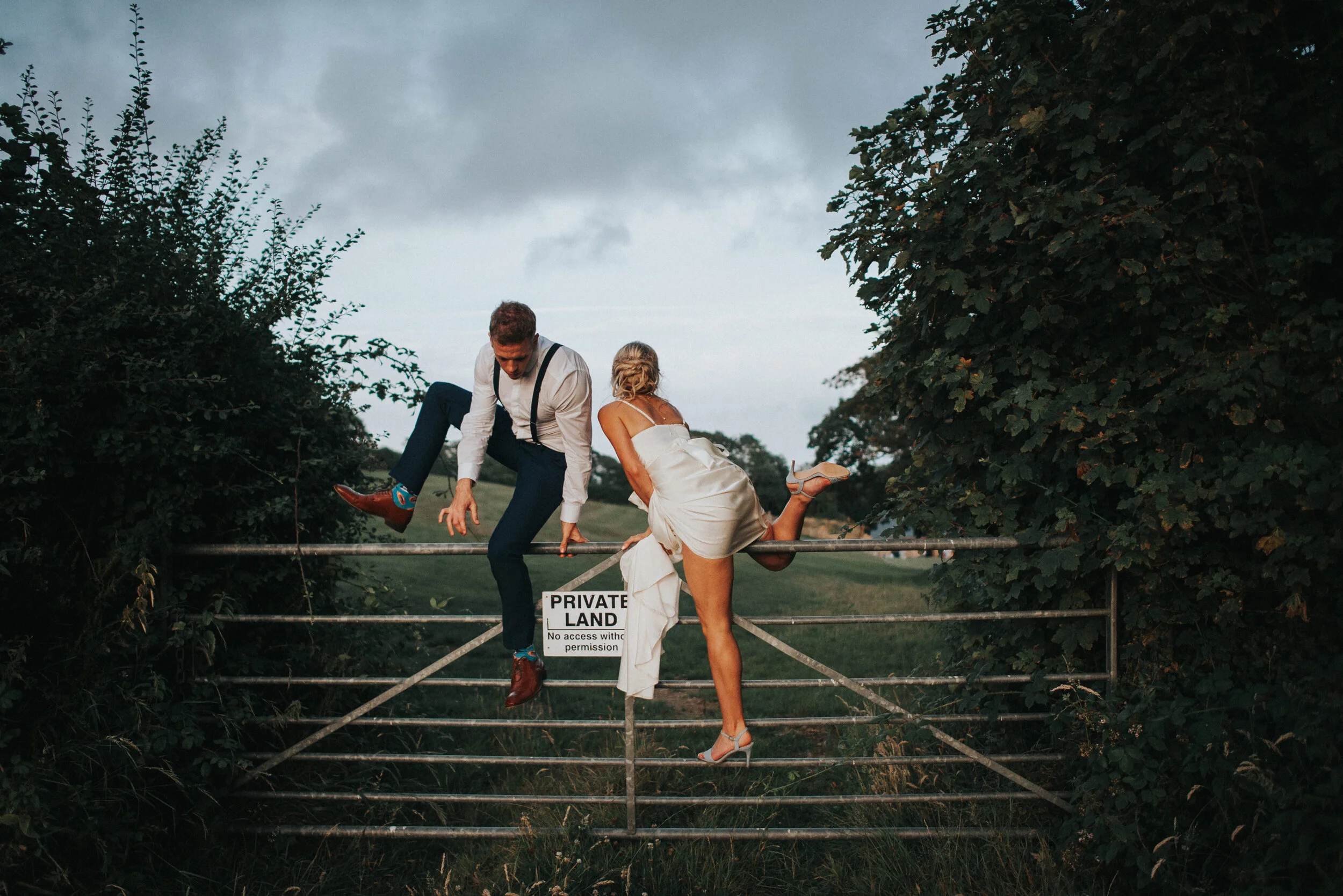 Bride and groom climbing over fence at Launcells Barton in Bude, captured by Cornwall wedding photographer Mark Shaw Photography