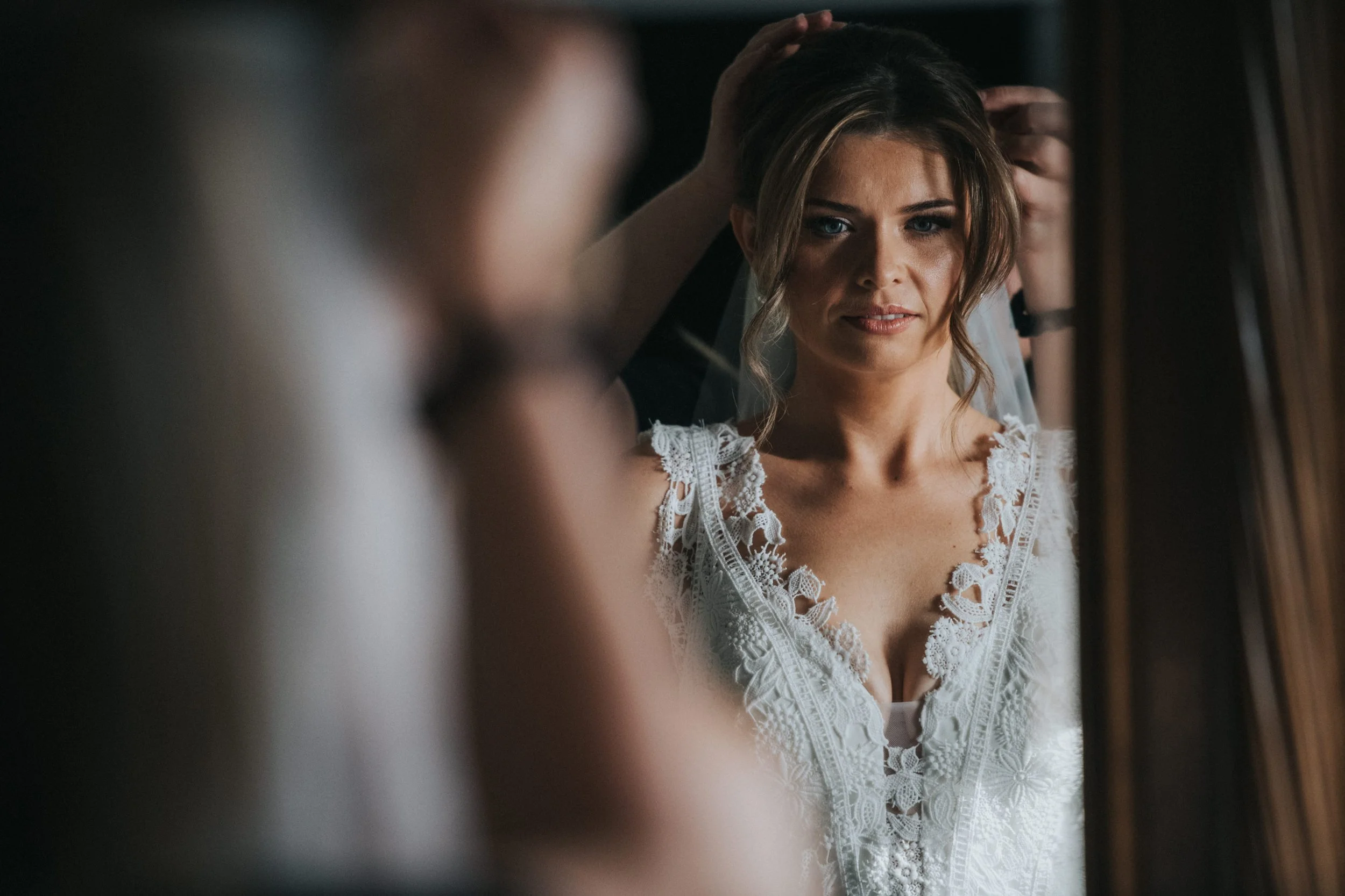 Bride getting ready at Fowey Hotel in Cornwall, wearing a white lace dress, looking in the mirror shortly before getting married.