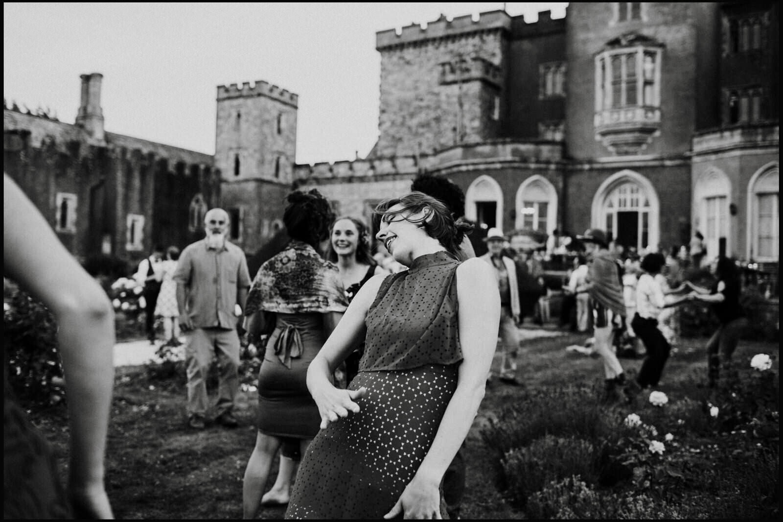 People dancing and socializing outdoors in front of a large castle-like building.