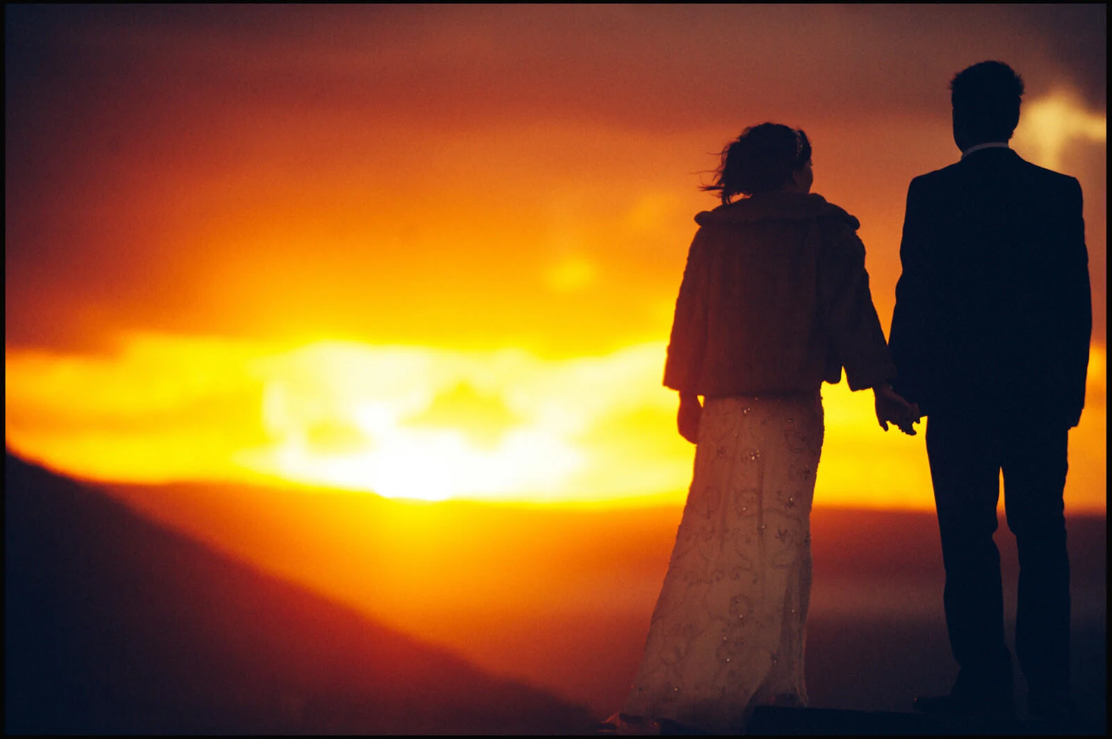 Silhouettes of a woman and a man holding hands, walking against a vivid sunset sky.