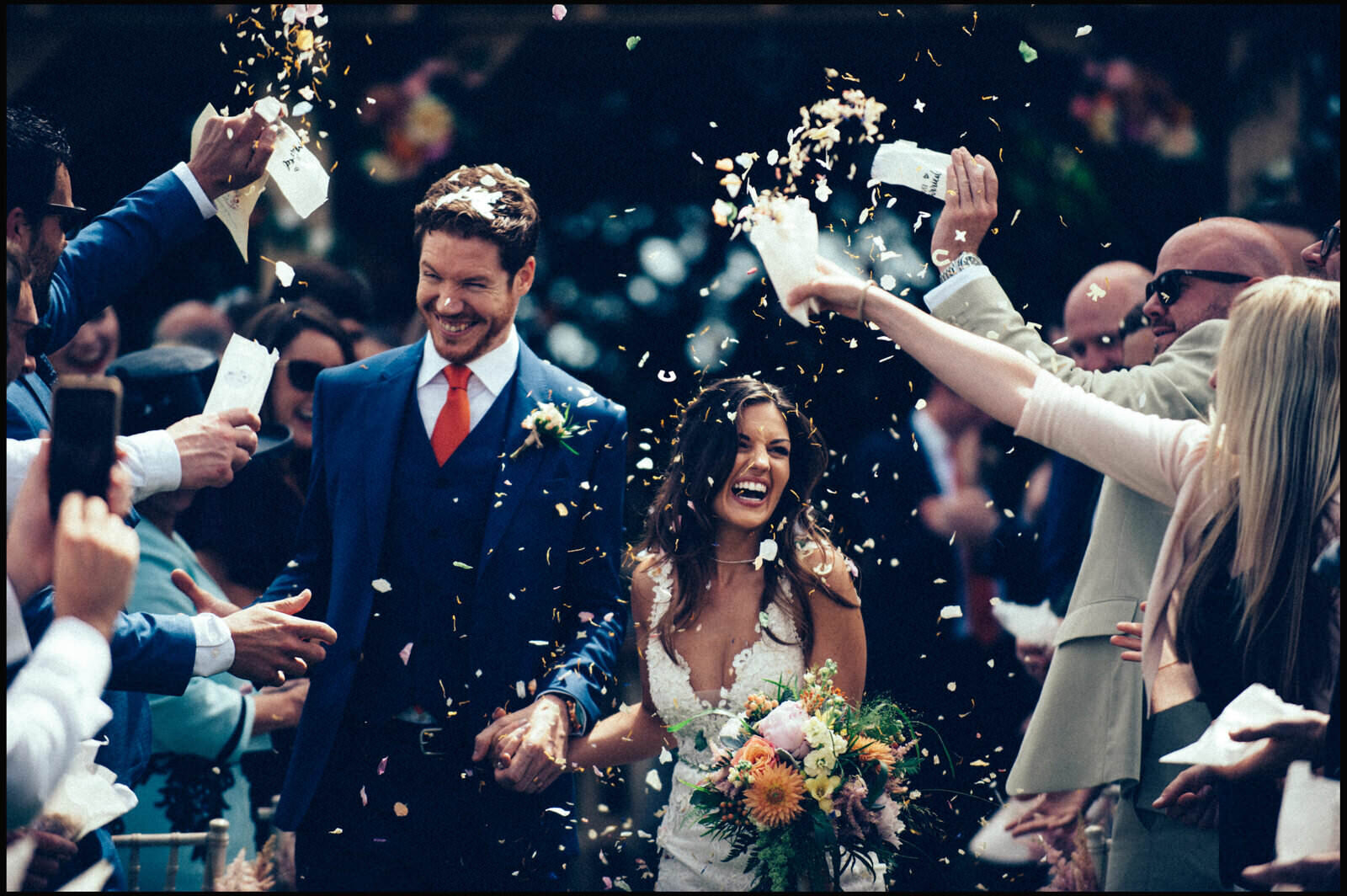 Bride and groom walking through a crowd of friends and family throwing confetti during their wedding celebration.
