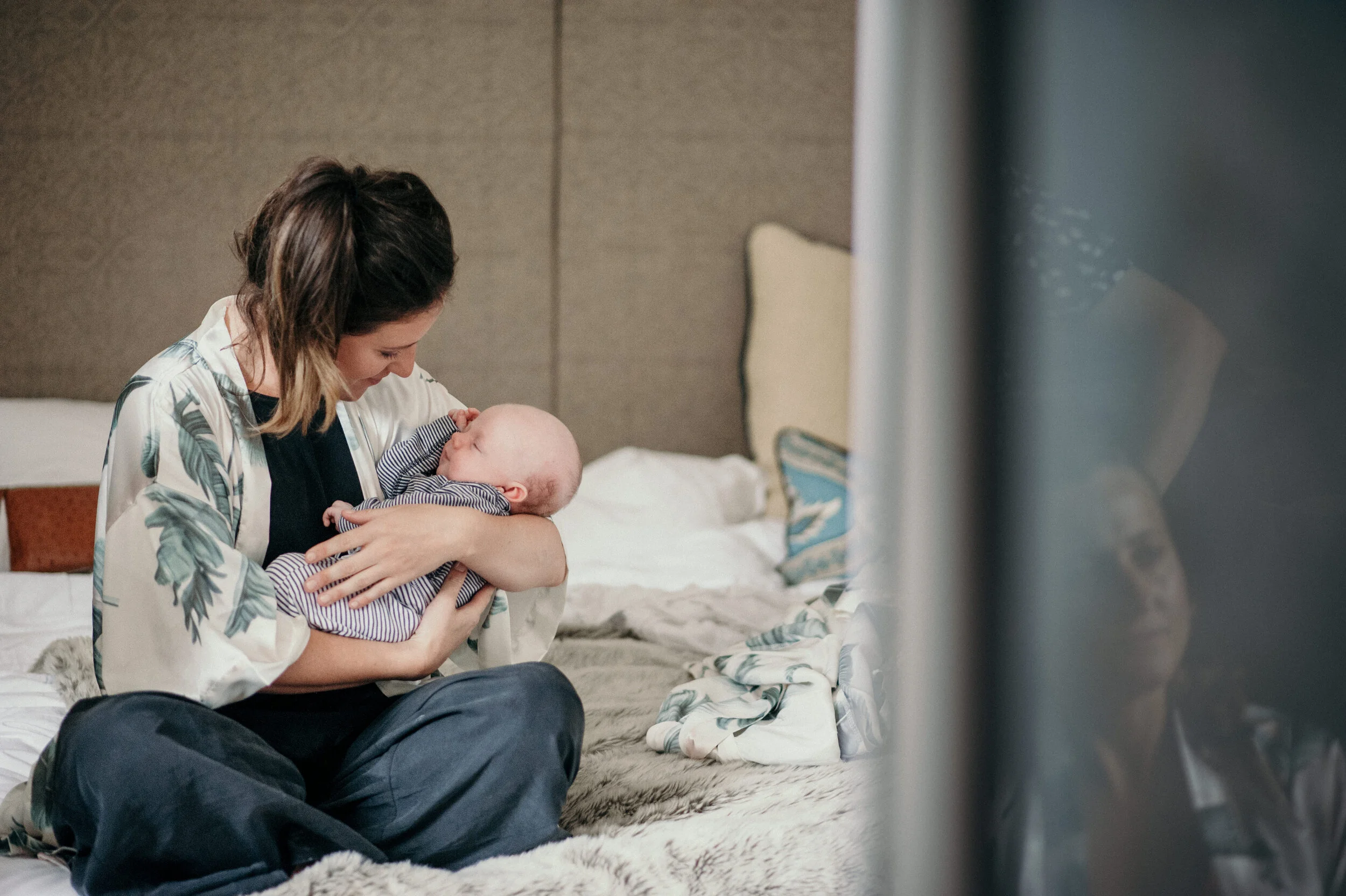 A woman holding a baby and looking at the baby in a bedroom.