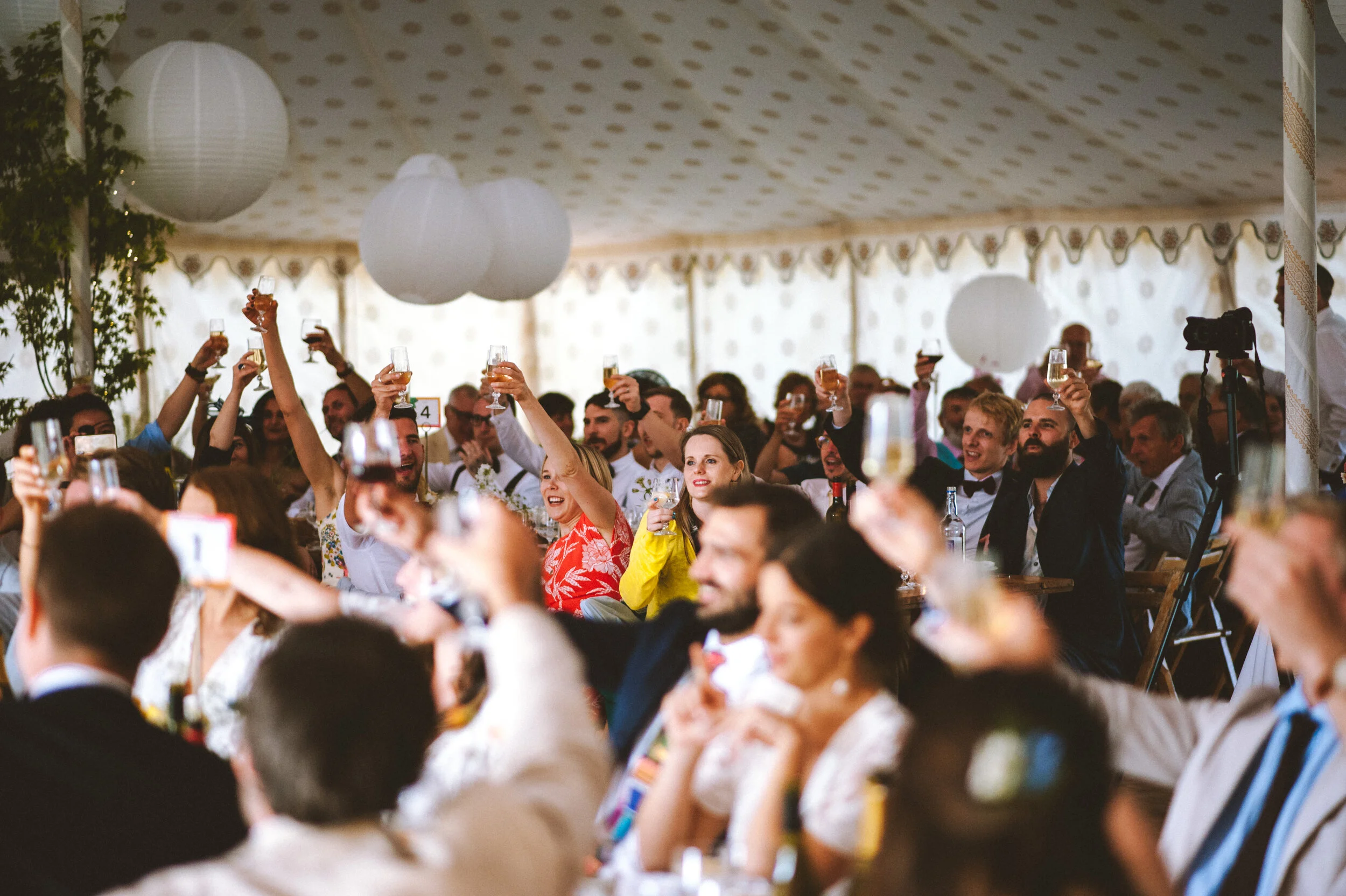 People at a celebration or wedding toast, holding champagne glasses inside a decorated tent.