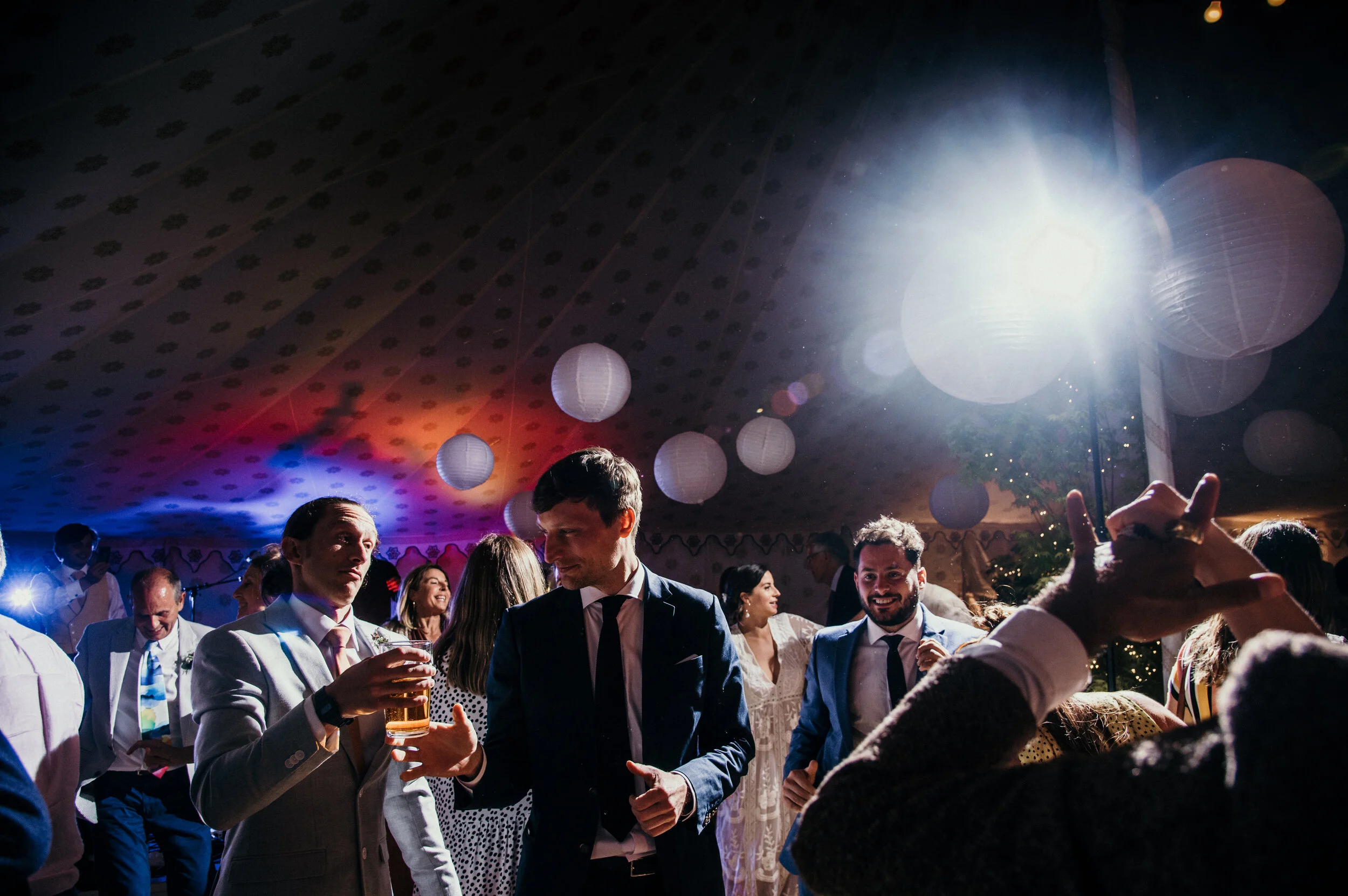 People dancing and socializing at a lively indoor party with decorative paper lanterns and colorful lighting.
