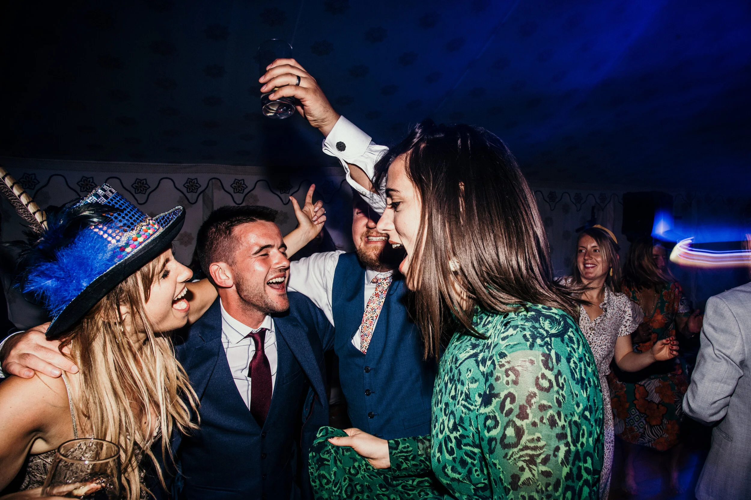 People celebrating and dancing at a party with one person wearing a colorful, bejeweled hat with feathers.