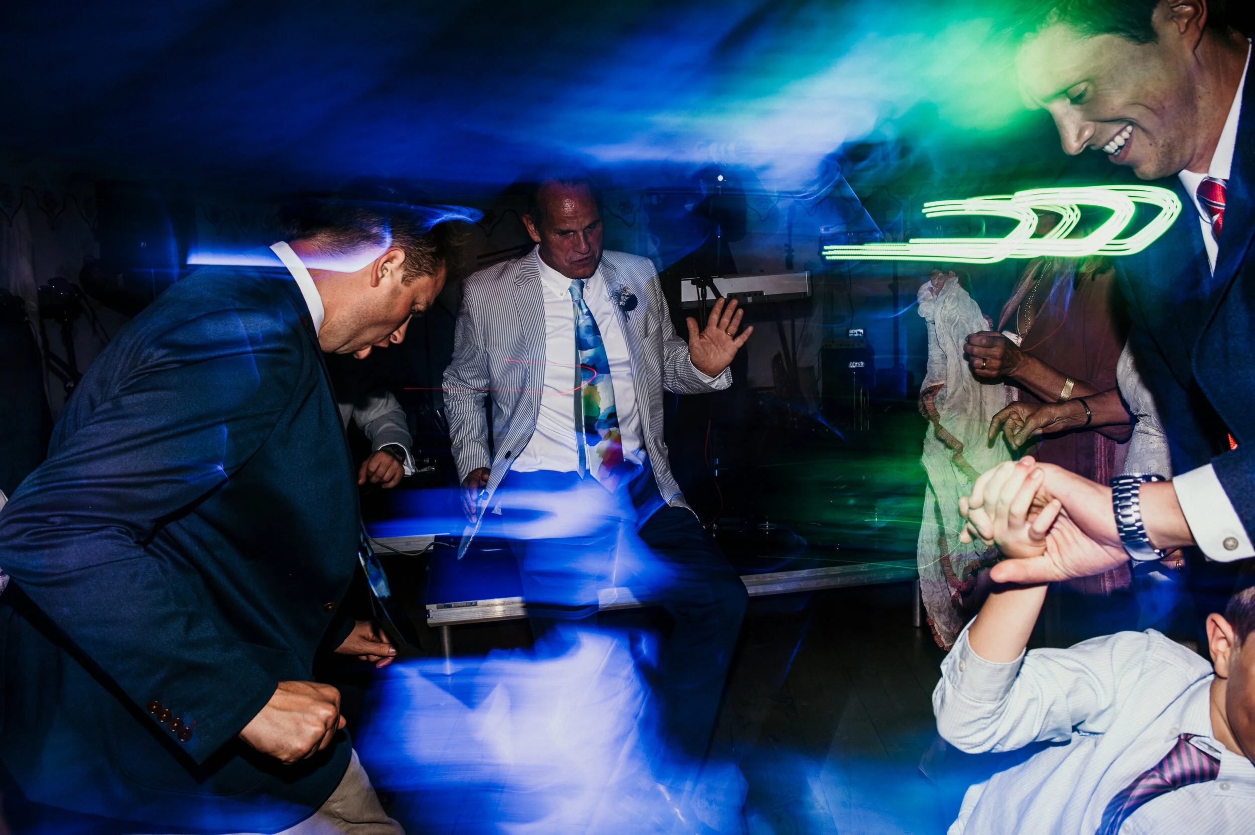 People dancing at a party with colorful lights and a DJ in the background.