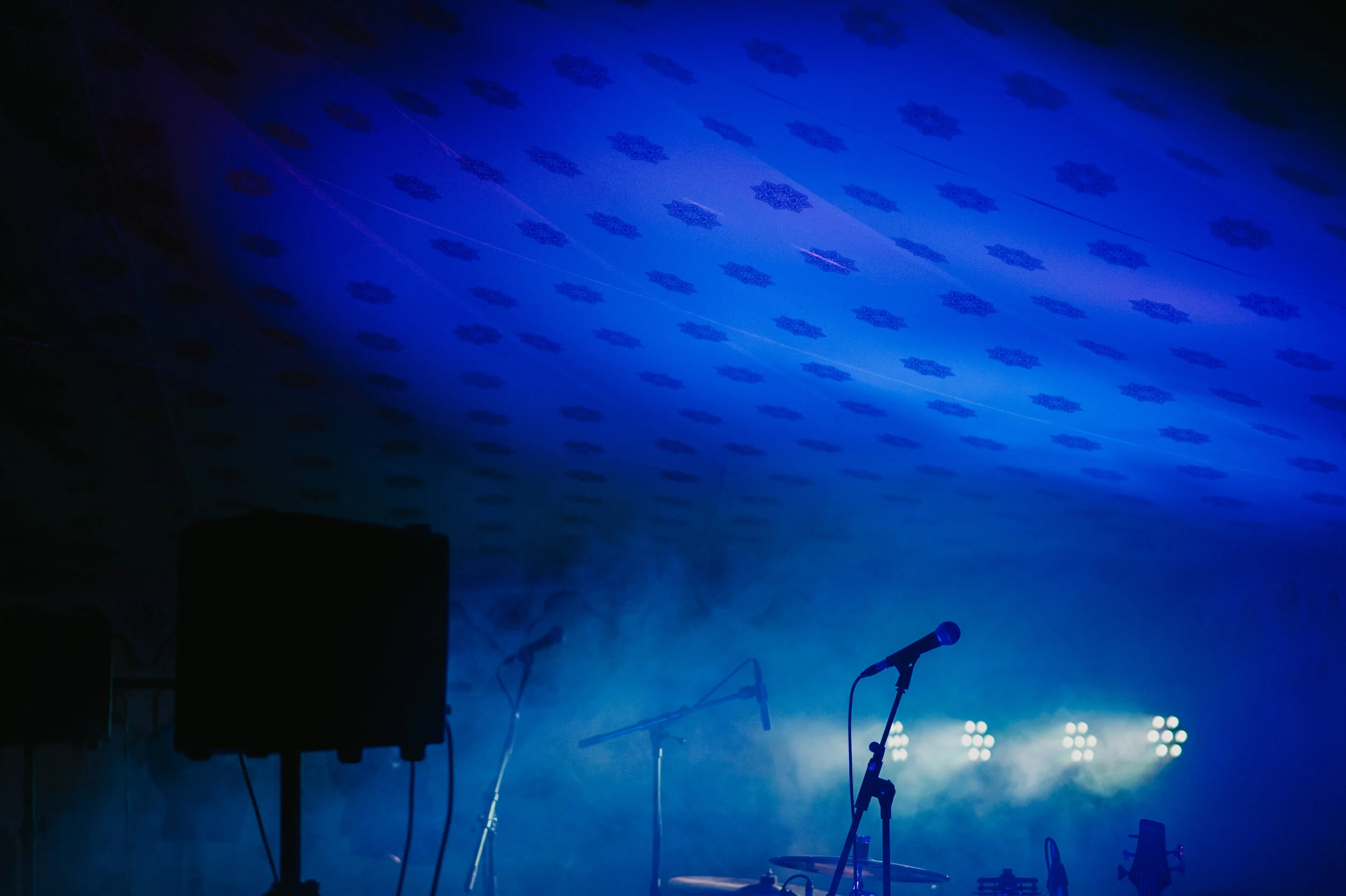 Stage setup with microphone on stand, speaker, and bright stage lights with fog, ready for a performance.