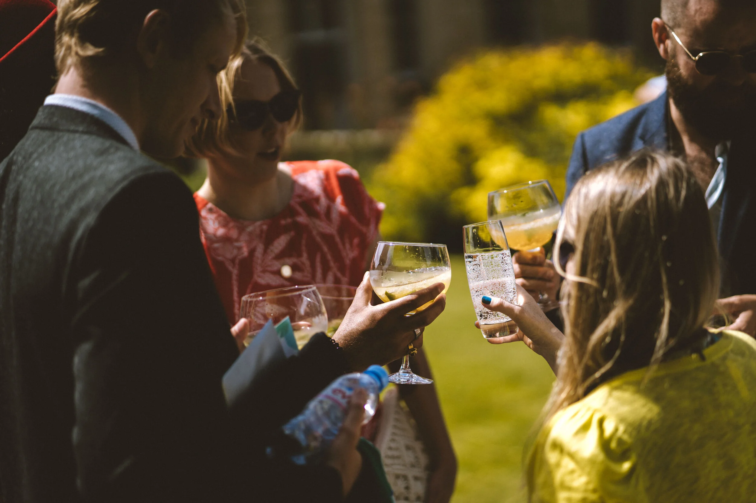 Group of people outdoors raising glasses with drinks during daytime celebration.