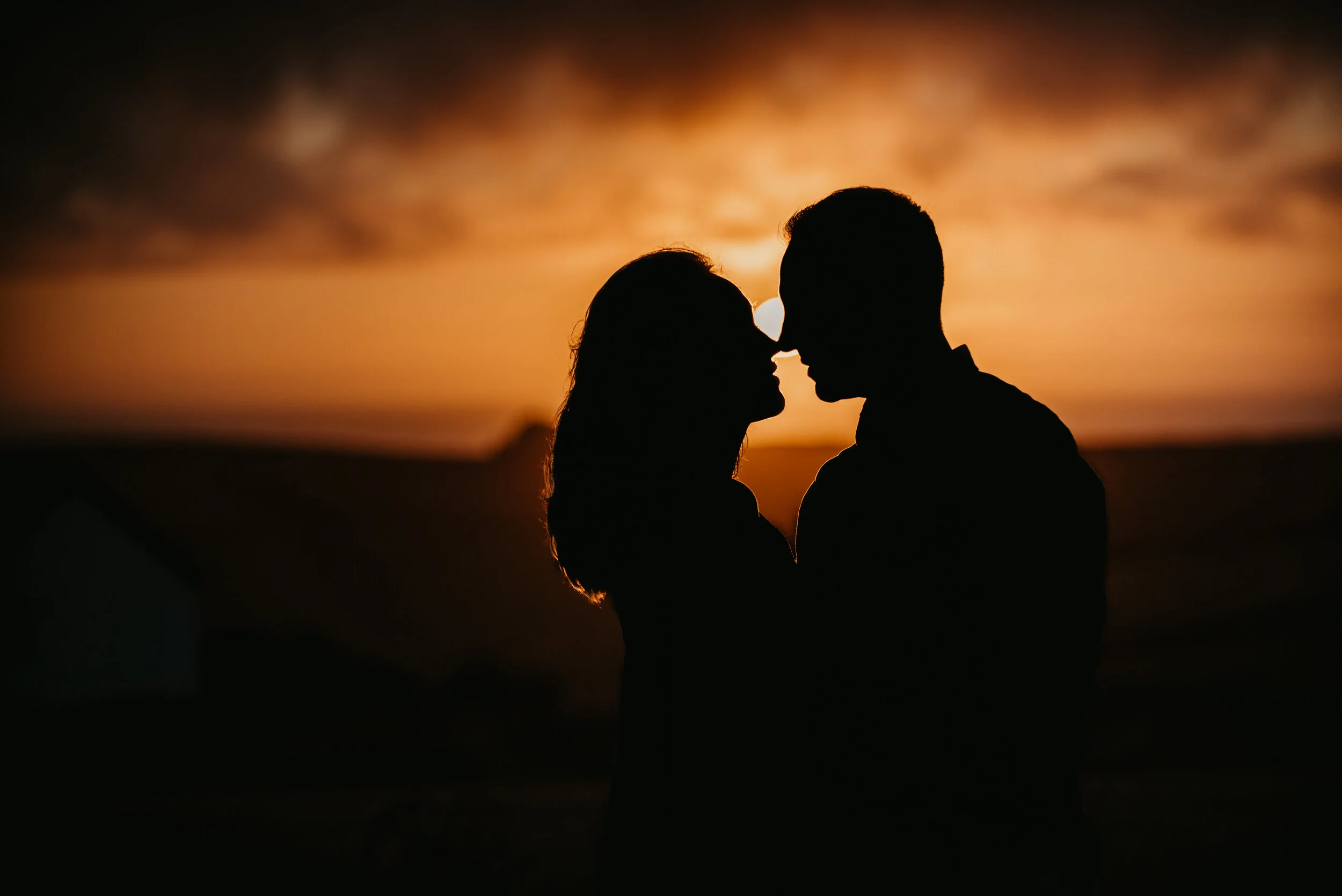 Silhouette of a couple facing each other closely at sunset on a beach.