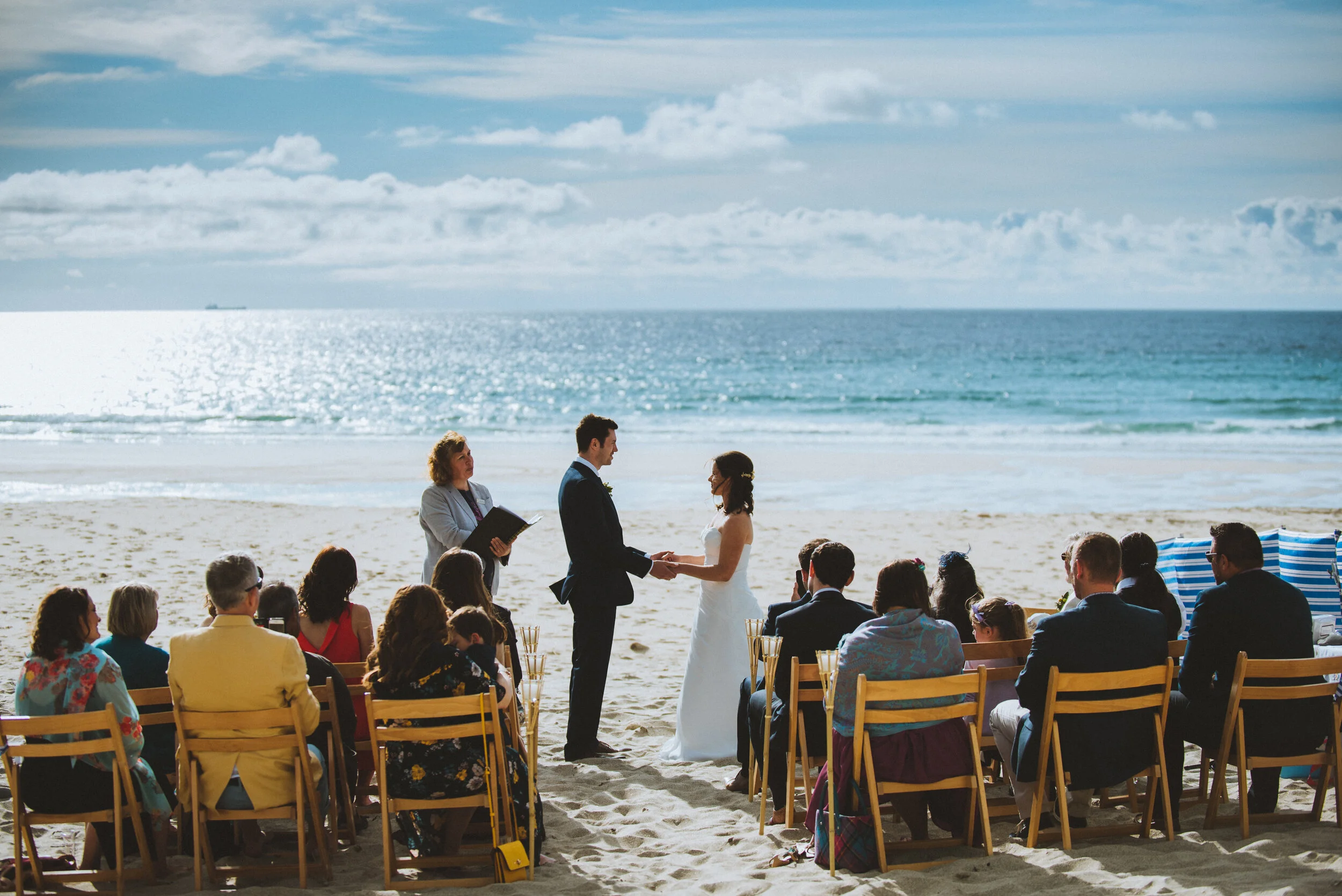 Couple getting married on a beach with guests seated in front of them and an ocean backdrop.