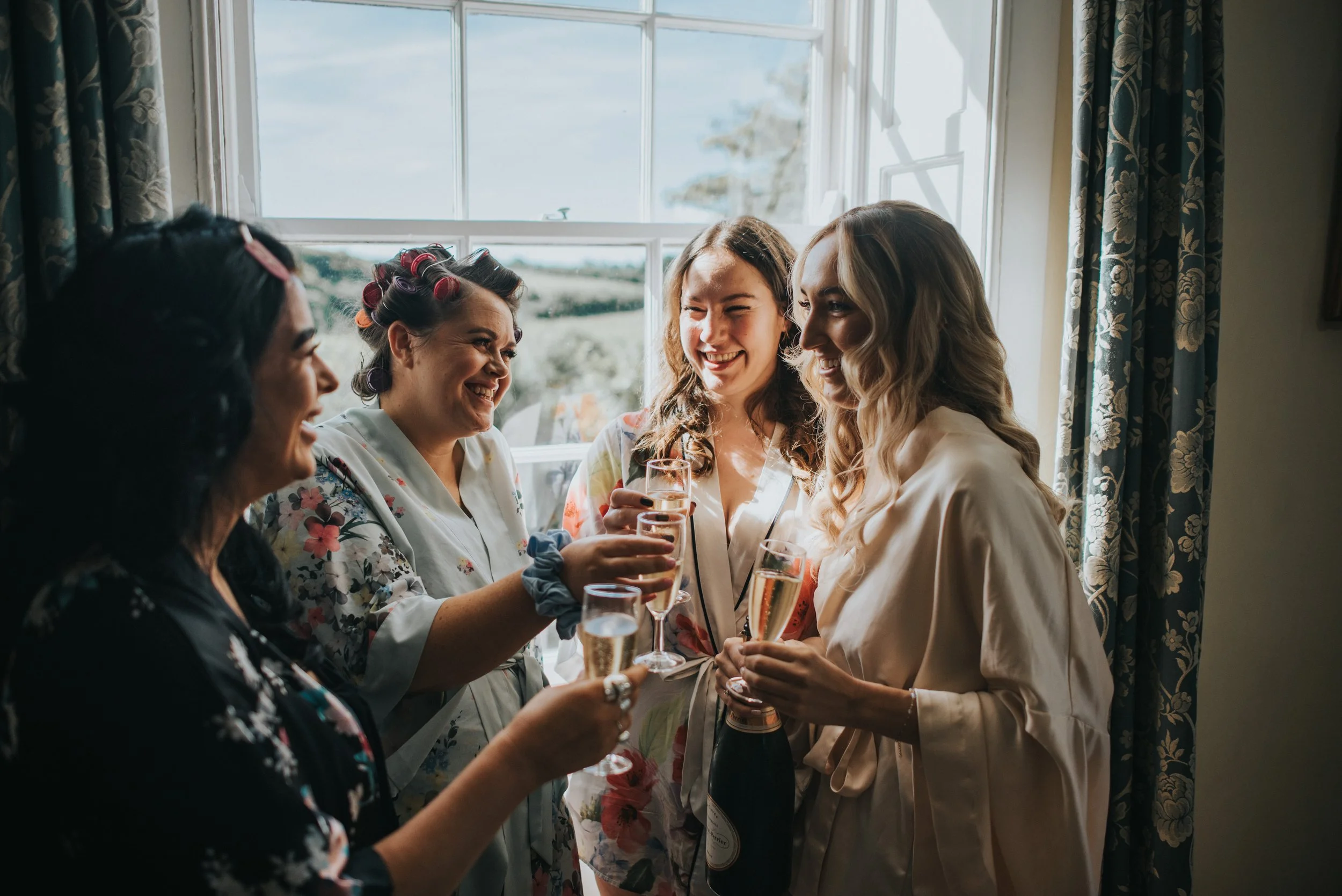 Four women in robes celebrating with glasses of champagne in front of a window.