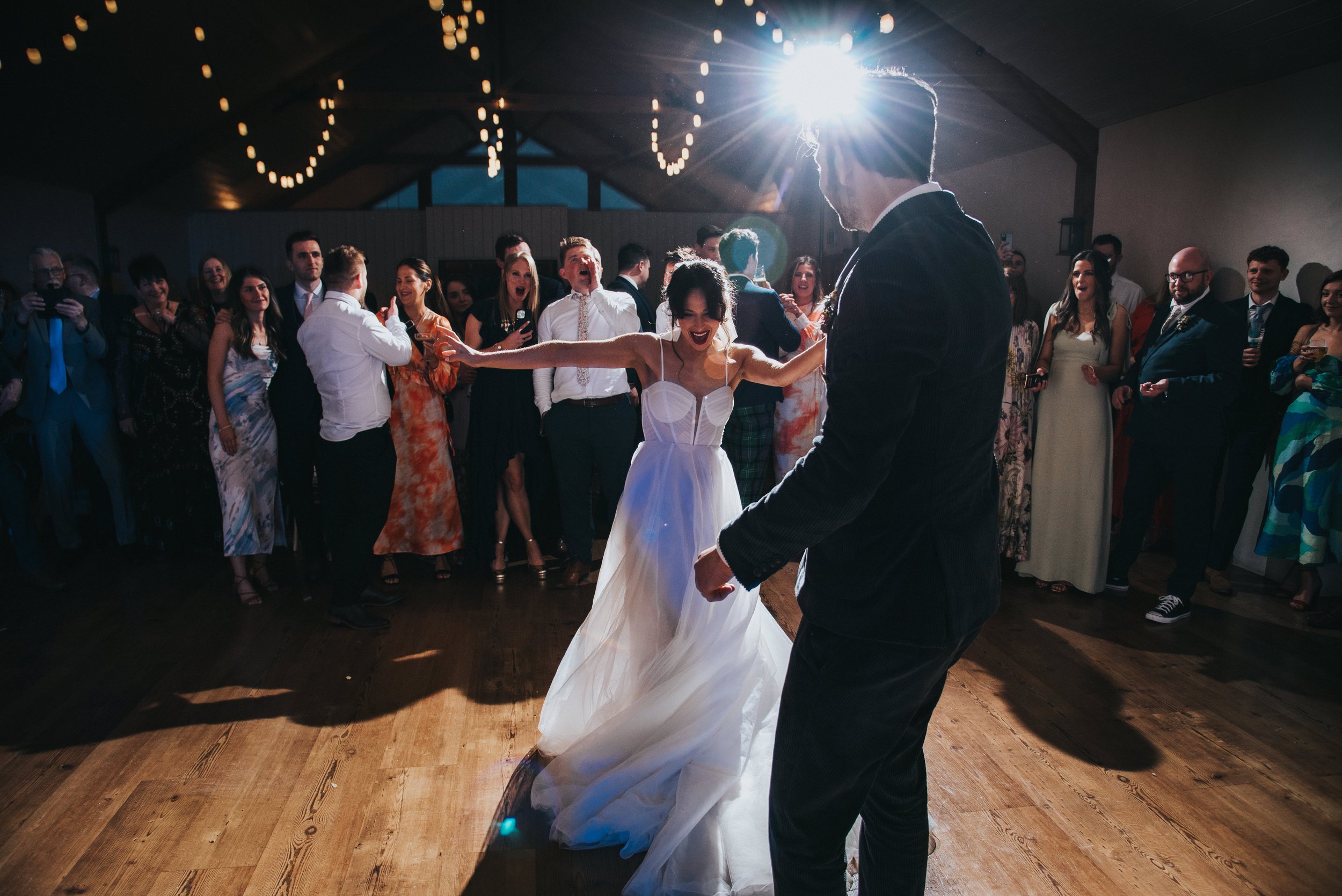 Bride and groom dancing at their wedding reception with guests watching, indoor venue with string lights