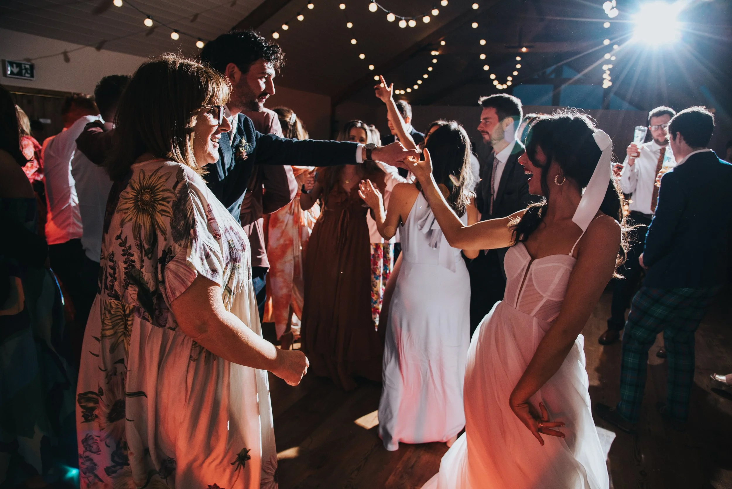 People dancing at a wedding reception under string lights with a bright light shining from the top right corner.