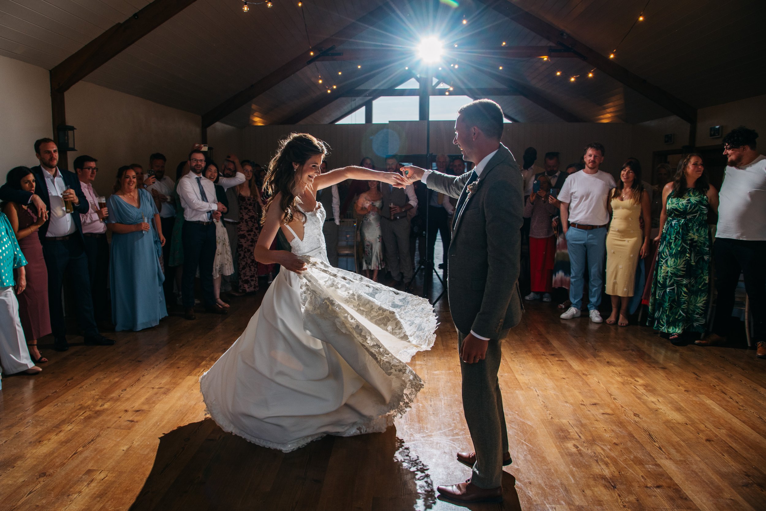 Couple dancing at their wedding reception with guests watching in the background inside a rustic wooden venue.