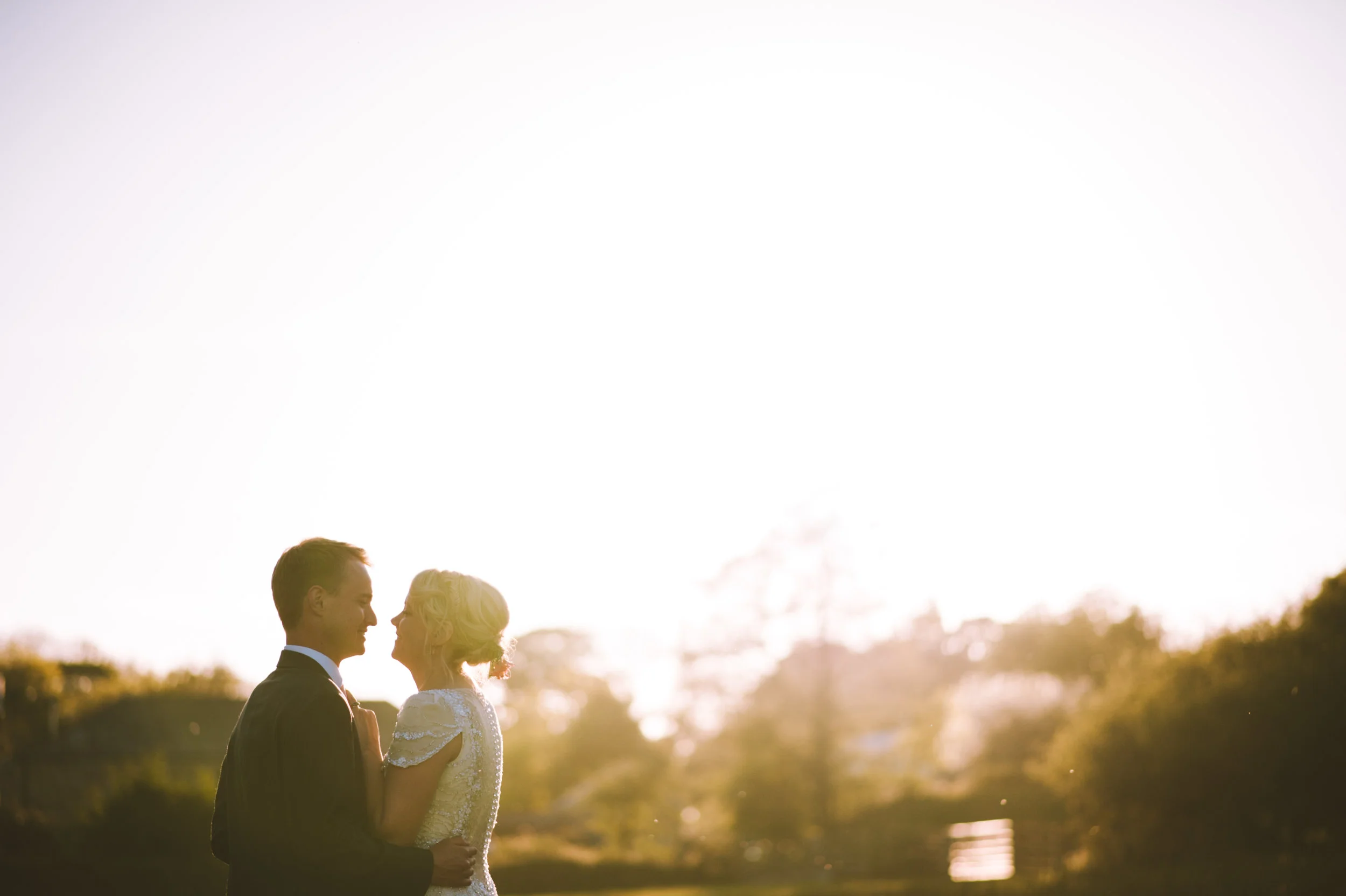 A couple on their wedding day standing close and gazing at each other during sunset outdoors.