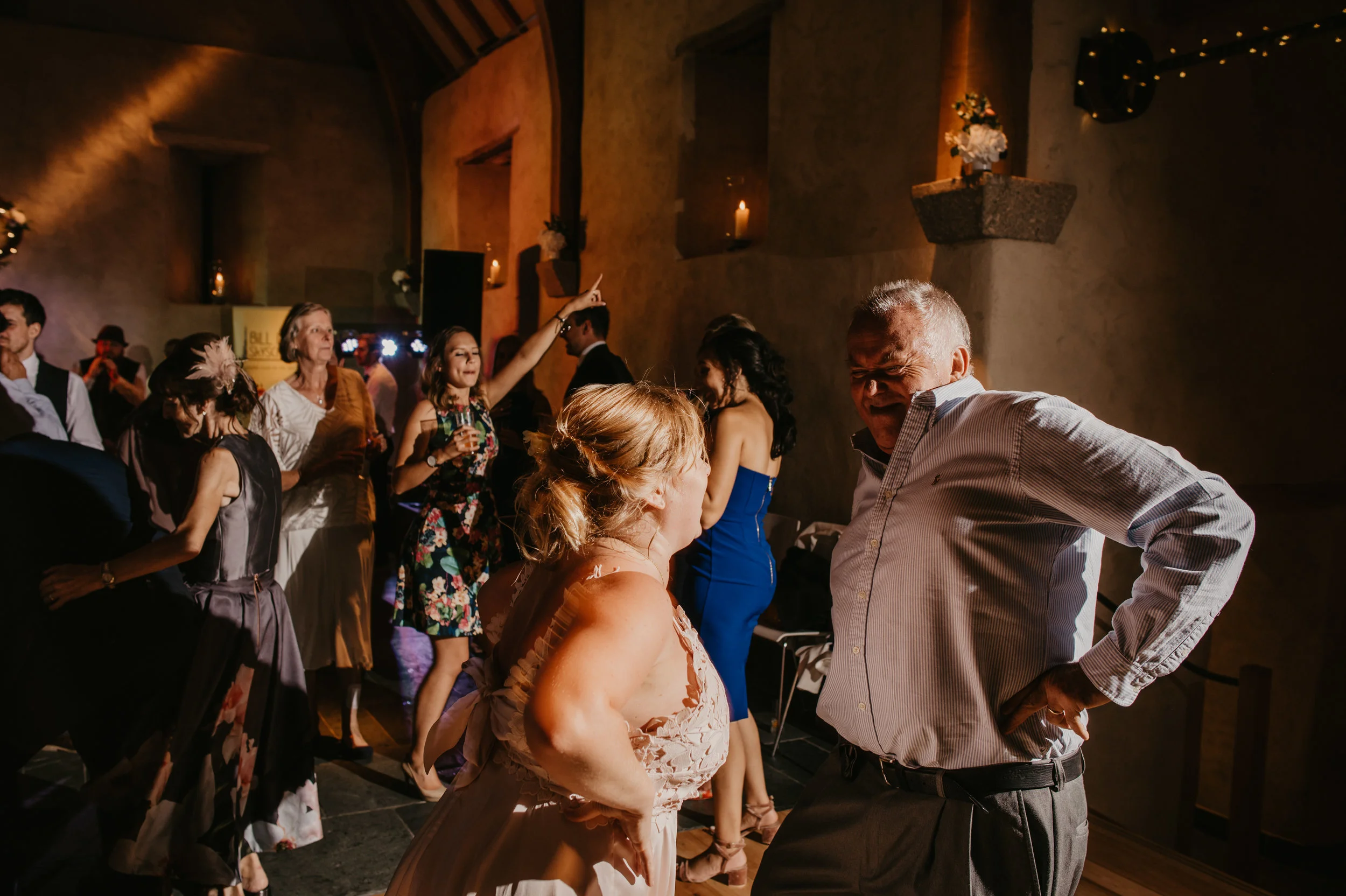 People dancing and socializing at an indoor celebration or party, with dim warm lighting and some candles.