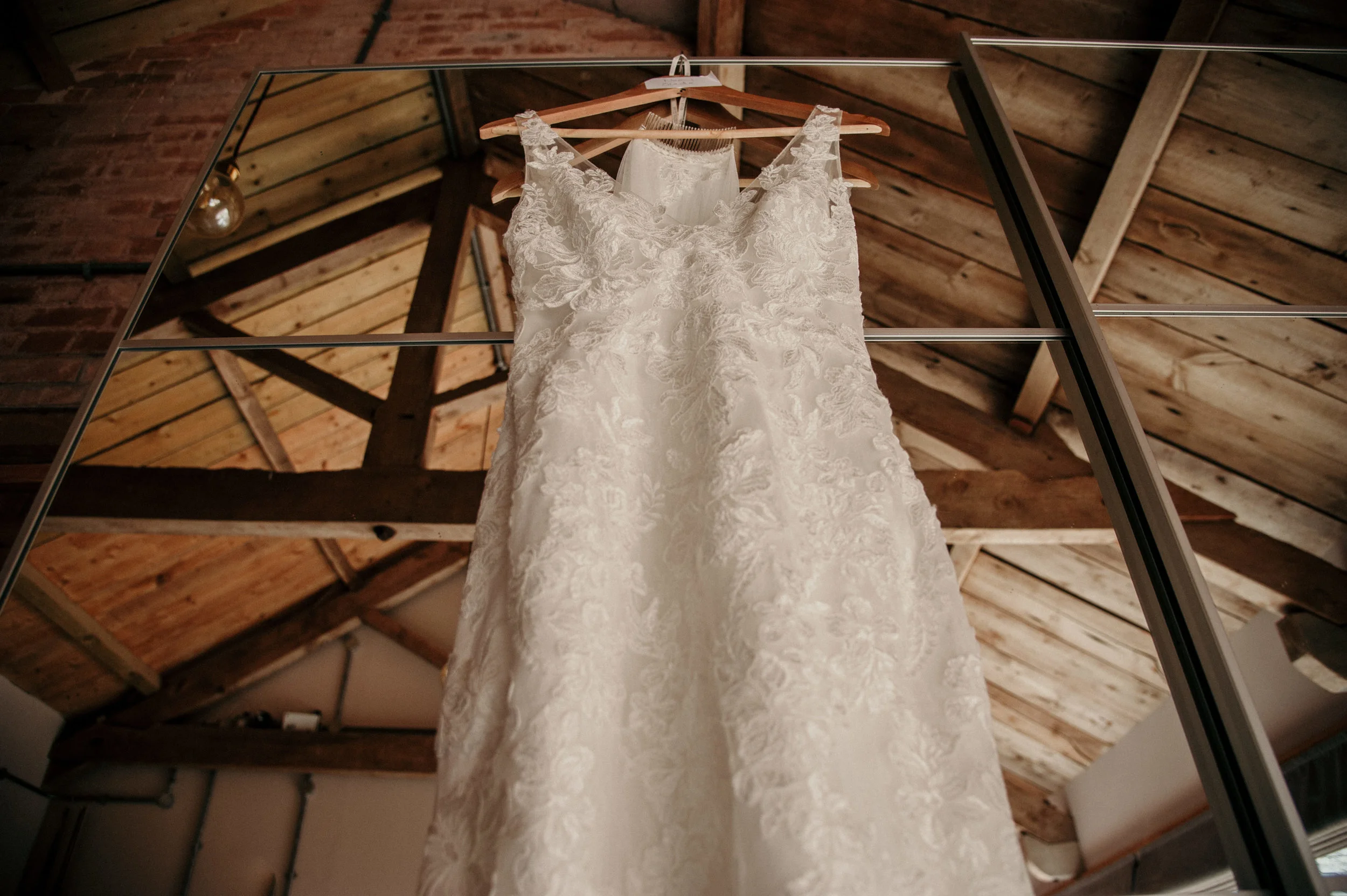 Wedding dress hanging on a wooden hanger, viewed from below, in a rustic wooden ceiling room.