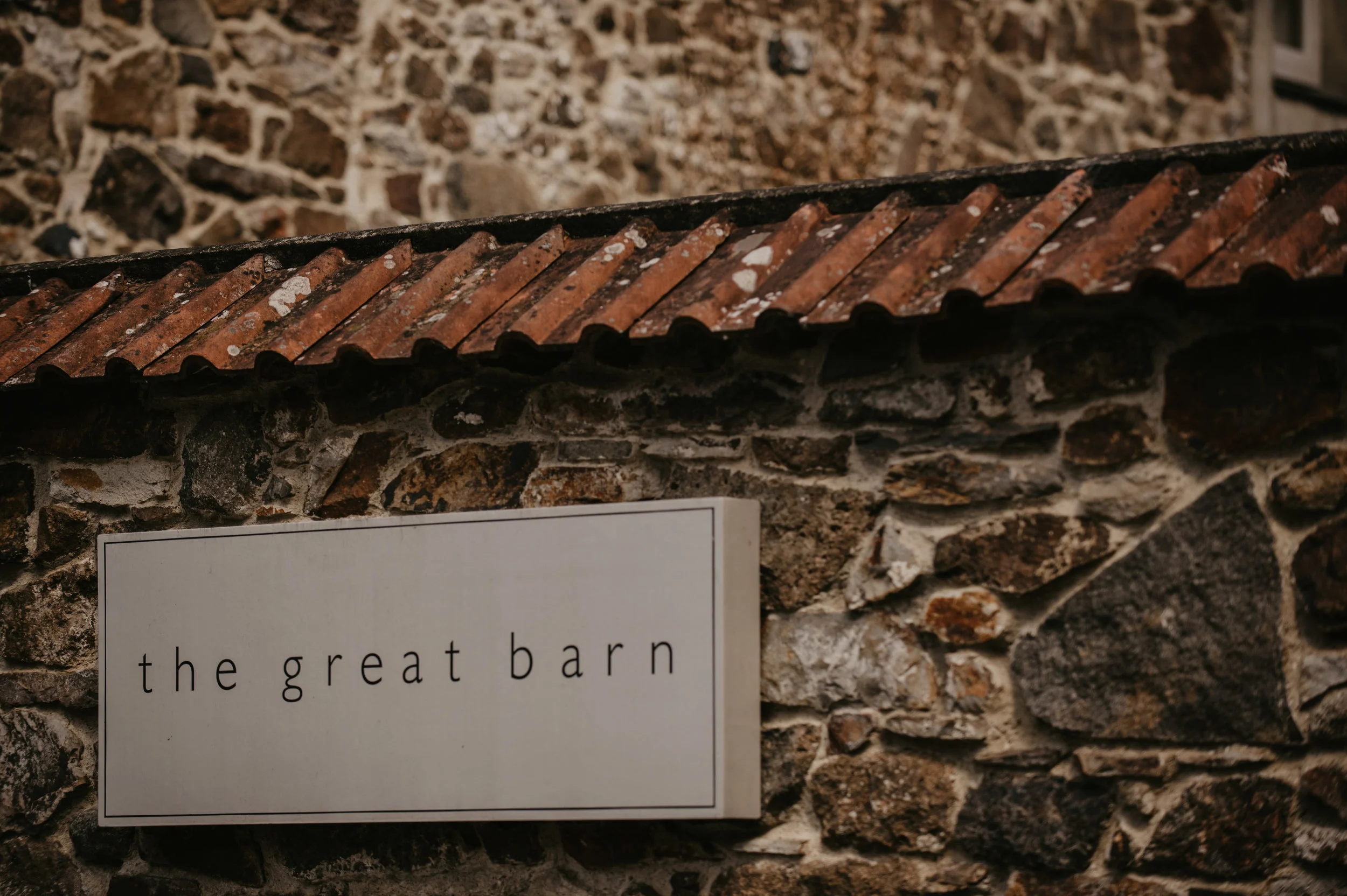 Stone wall with a small tiled roof and a sign that reads 'the great barn'