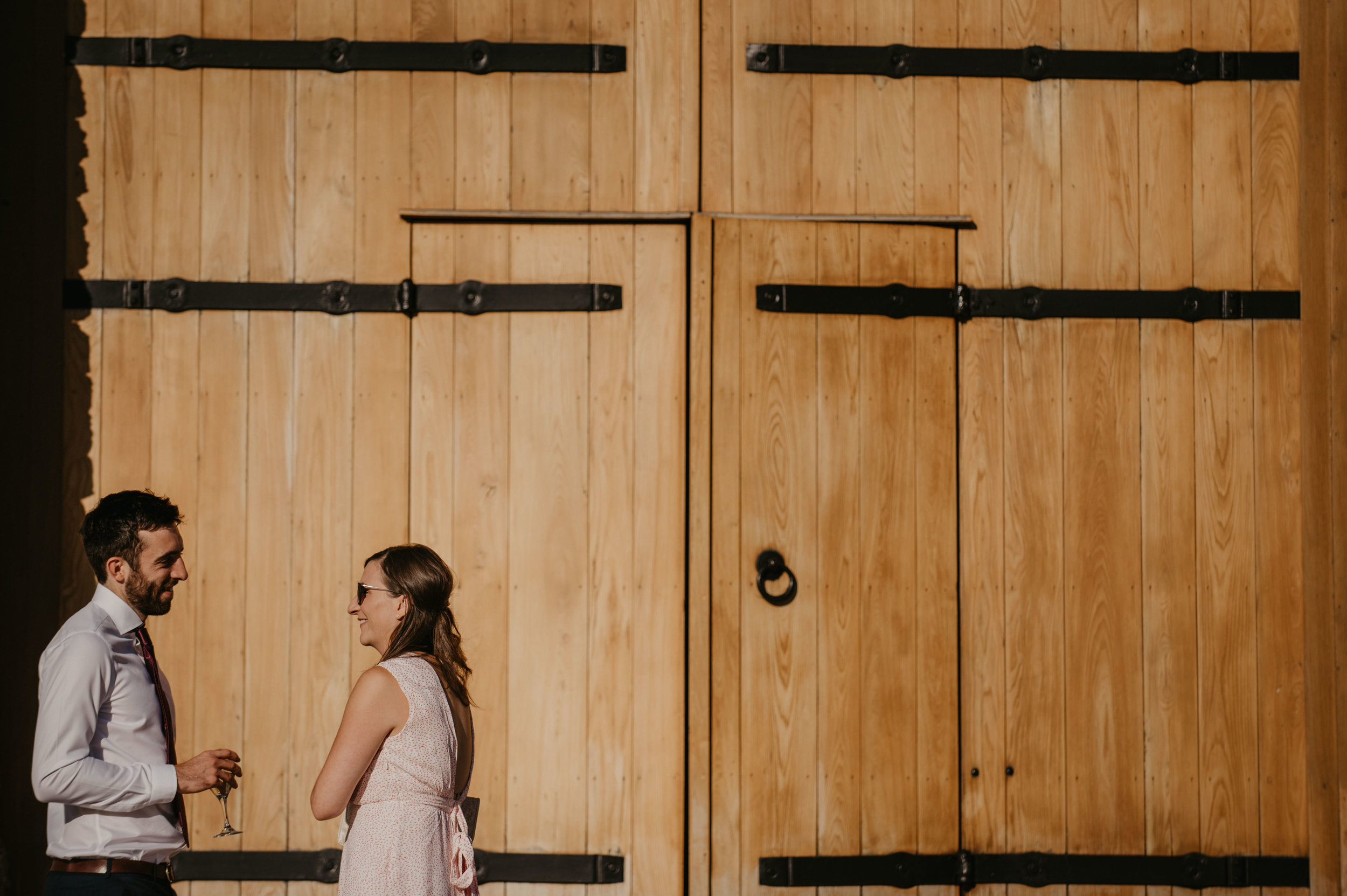 A man and woman in formal attire standing in front of a large wooden barn door, smiling and talking to each other.