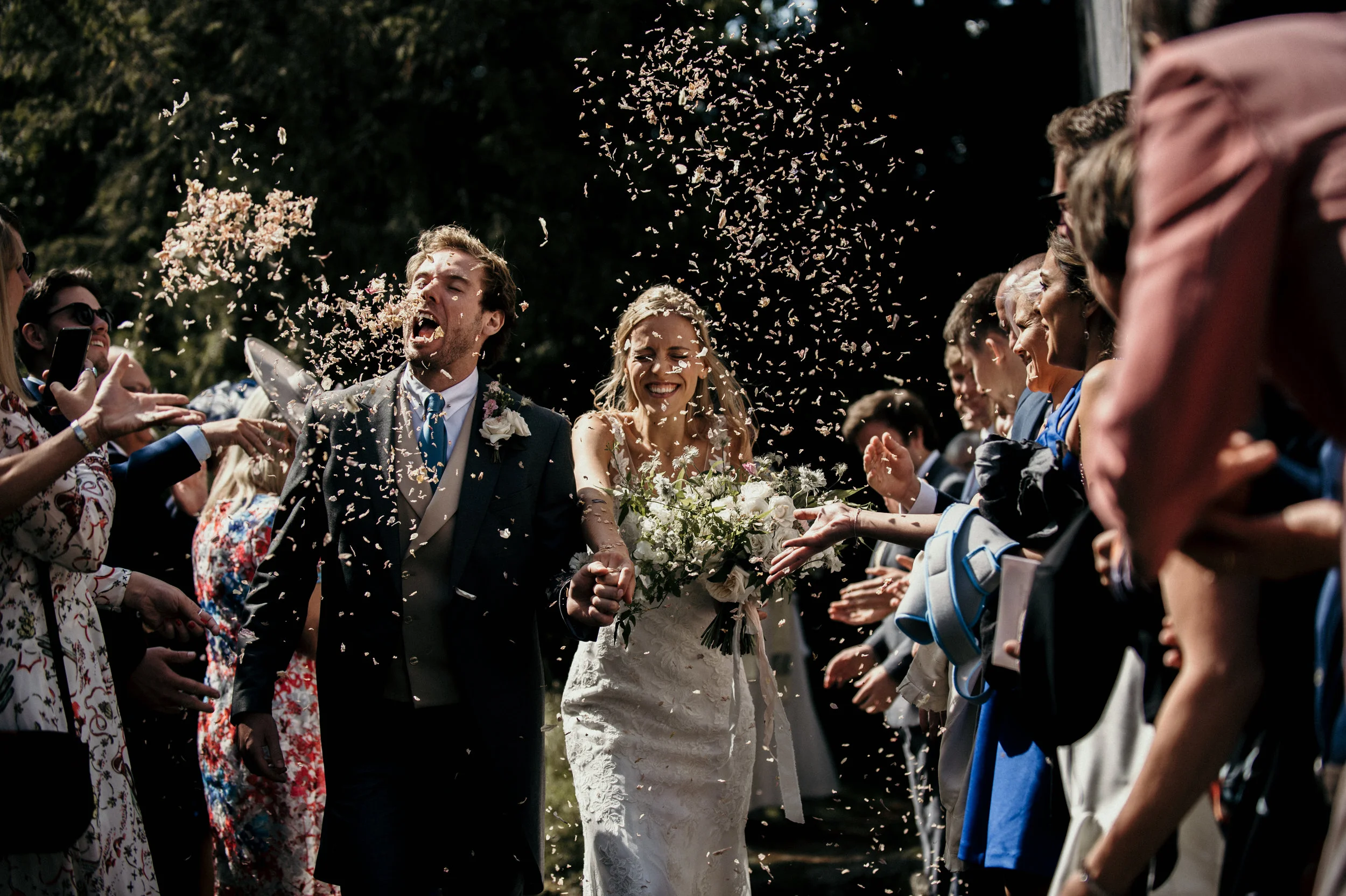 Bride and groom walking through crowd throwing rice at outdoor wedding.