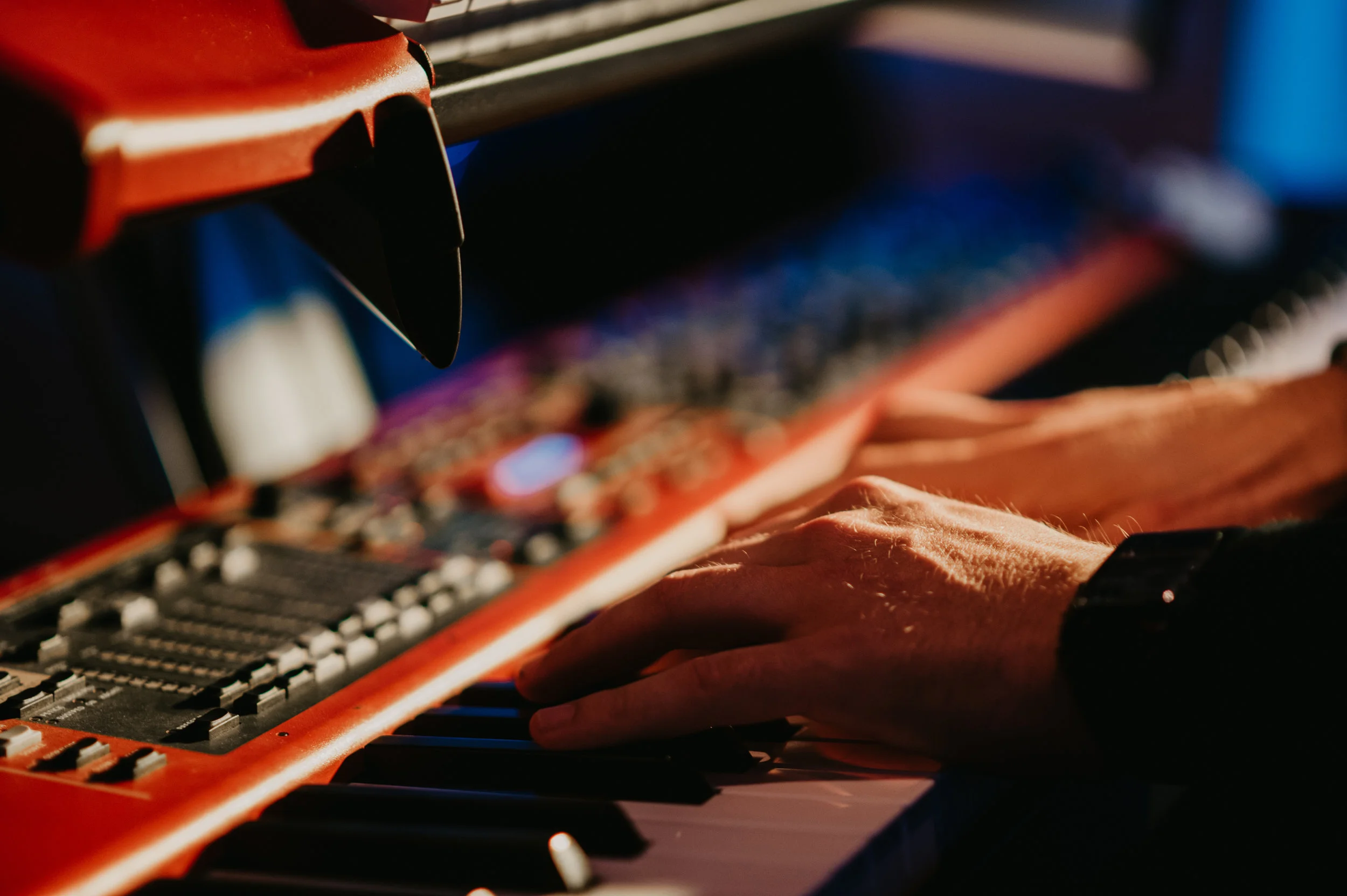 Close-up of a person's hand playing a red keyboard synthesizer with various controls and knobs