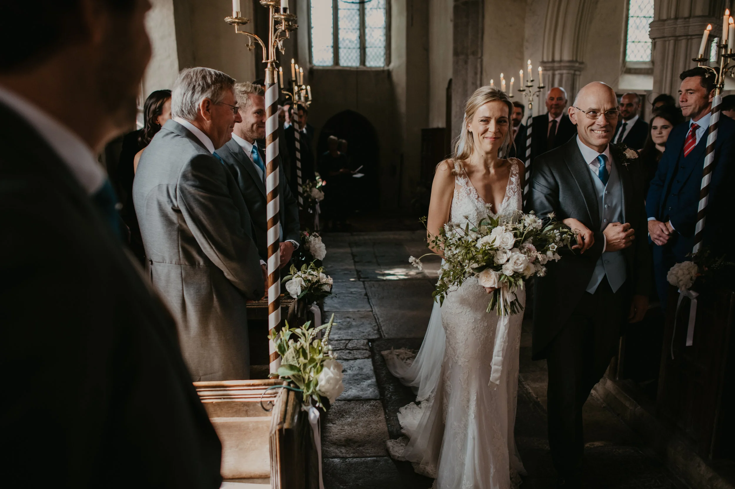 A bride walking down the aisle with a man in a church during her wedding ceremony, surrounded by guests, candles, and flower decorations.