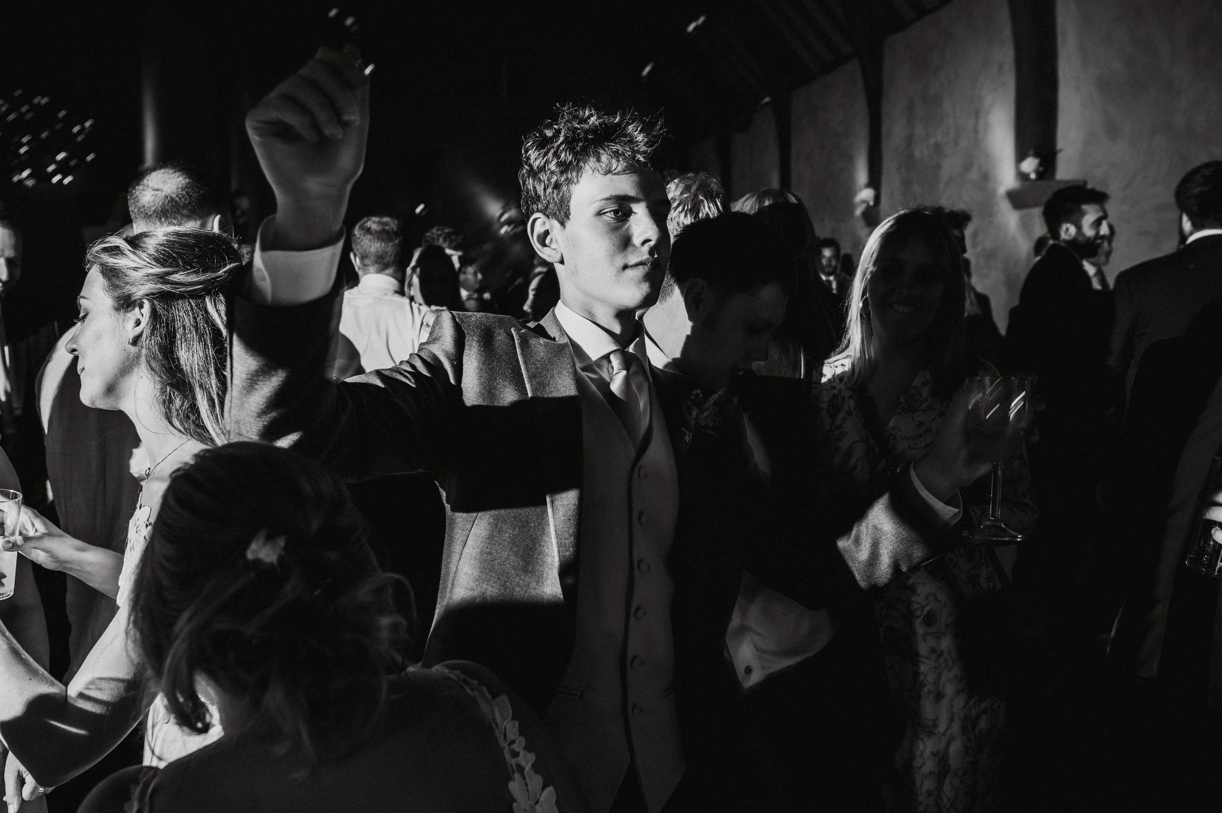 People at a social event or party, some holding drinks, in a dimly lit indoor venue with a festive atmosphere.