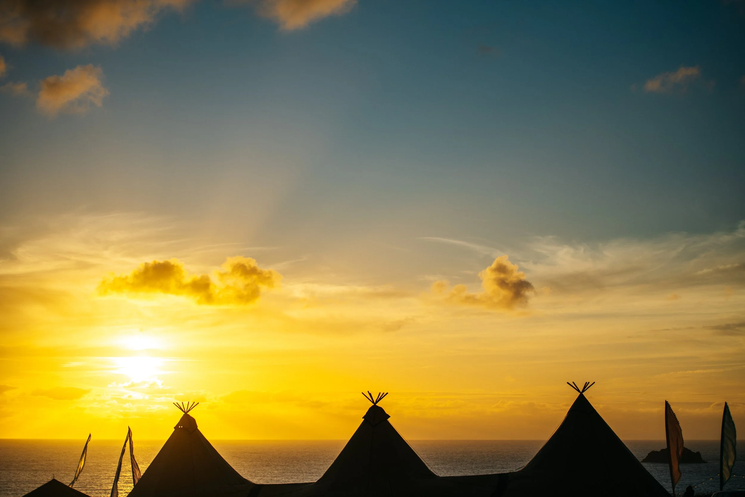 Romantic Cornwall marquee wedding with sunset over ocean with teepee silhouettes and clouds.