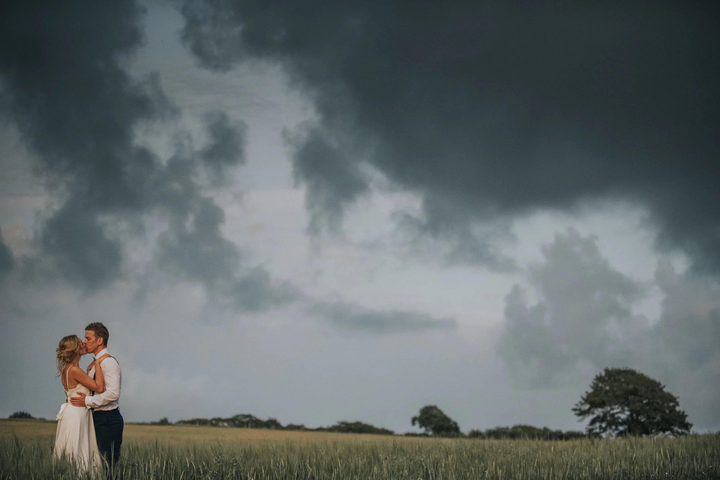 Couple kissing in farmers field at Launcells Barton in Cornwall with moody dark clouds.