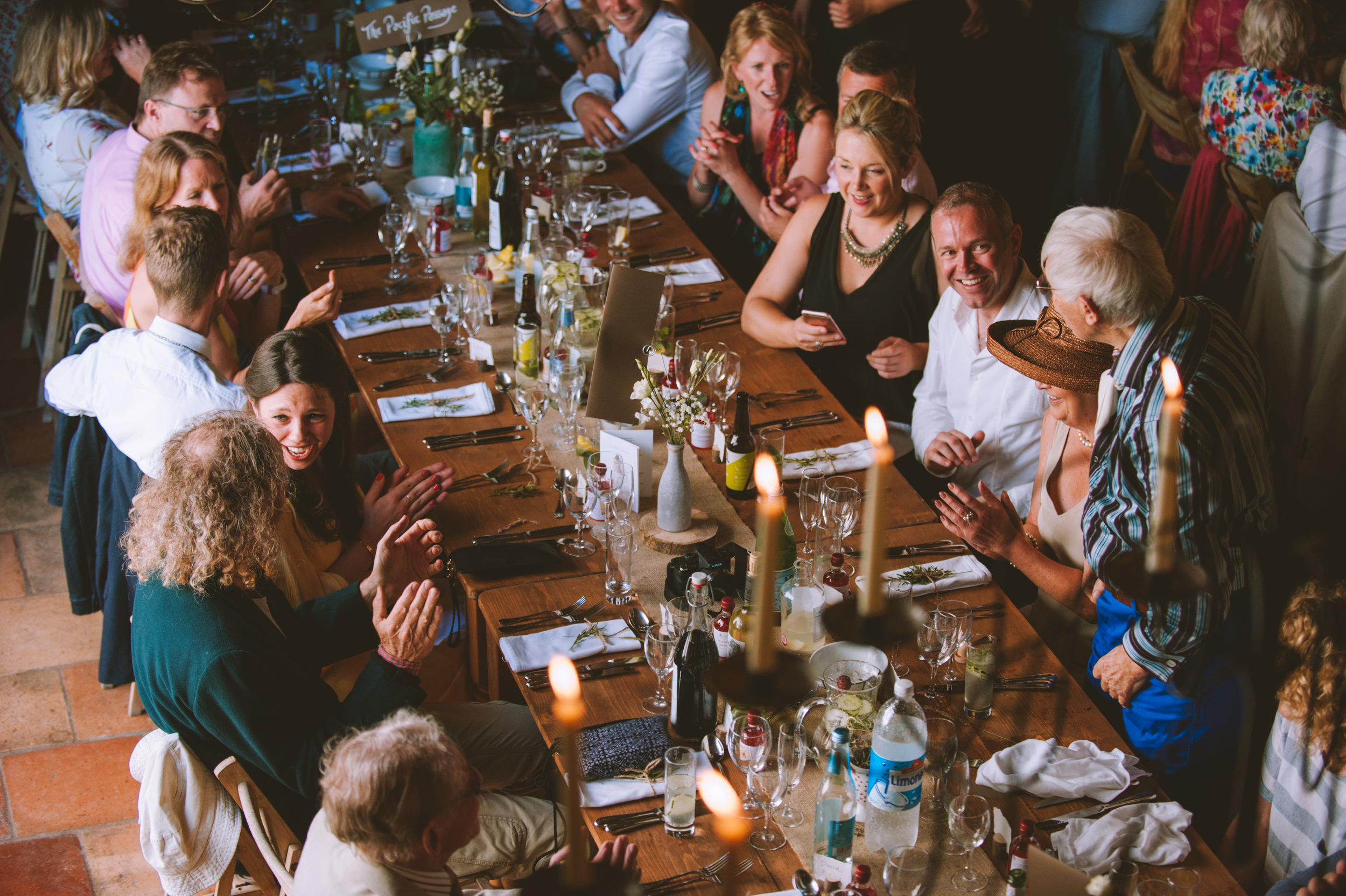 A large group of people gathered around a long dinner table, enjoying a celebration with food, drinks, and conversation in a well-lit room.