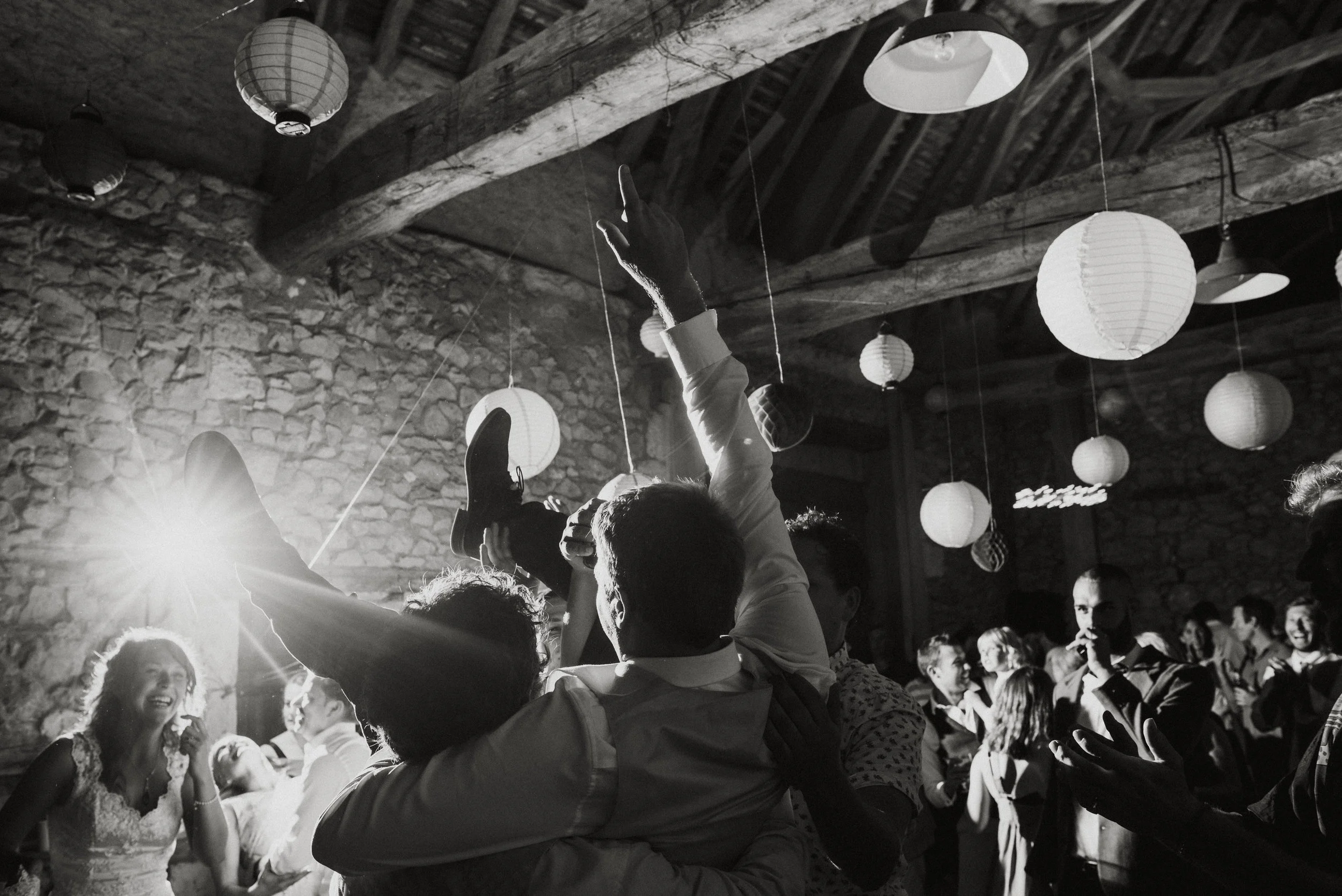 People dancing and celebrating at a party with hanging paper lanterns and rustic decor.